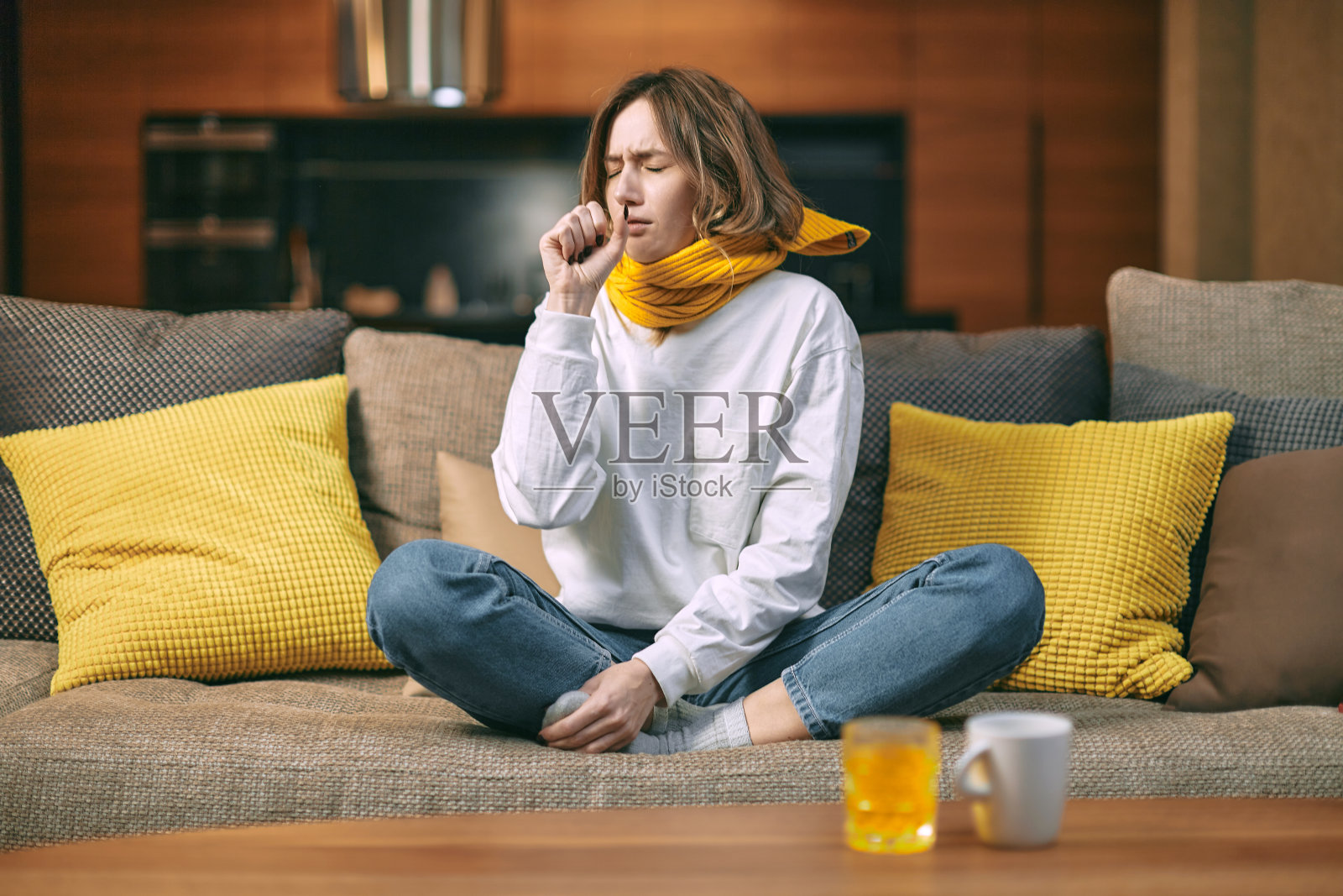 冷,感冒咳嗽。生病的女人坐在家里的沙发上咳嗽，喝着一杯热饮，一杯含有维生素c的药照片摄影图片