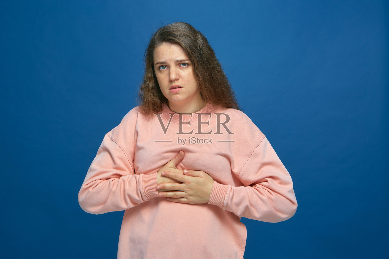 生病的年轻女孩，20多岁，紧握着胸部，遭受着心脏疼痛或乳房疼痛，肋间神经痛蓝色工作室背景照片摄影图片