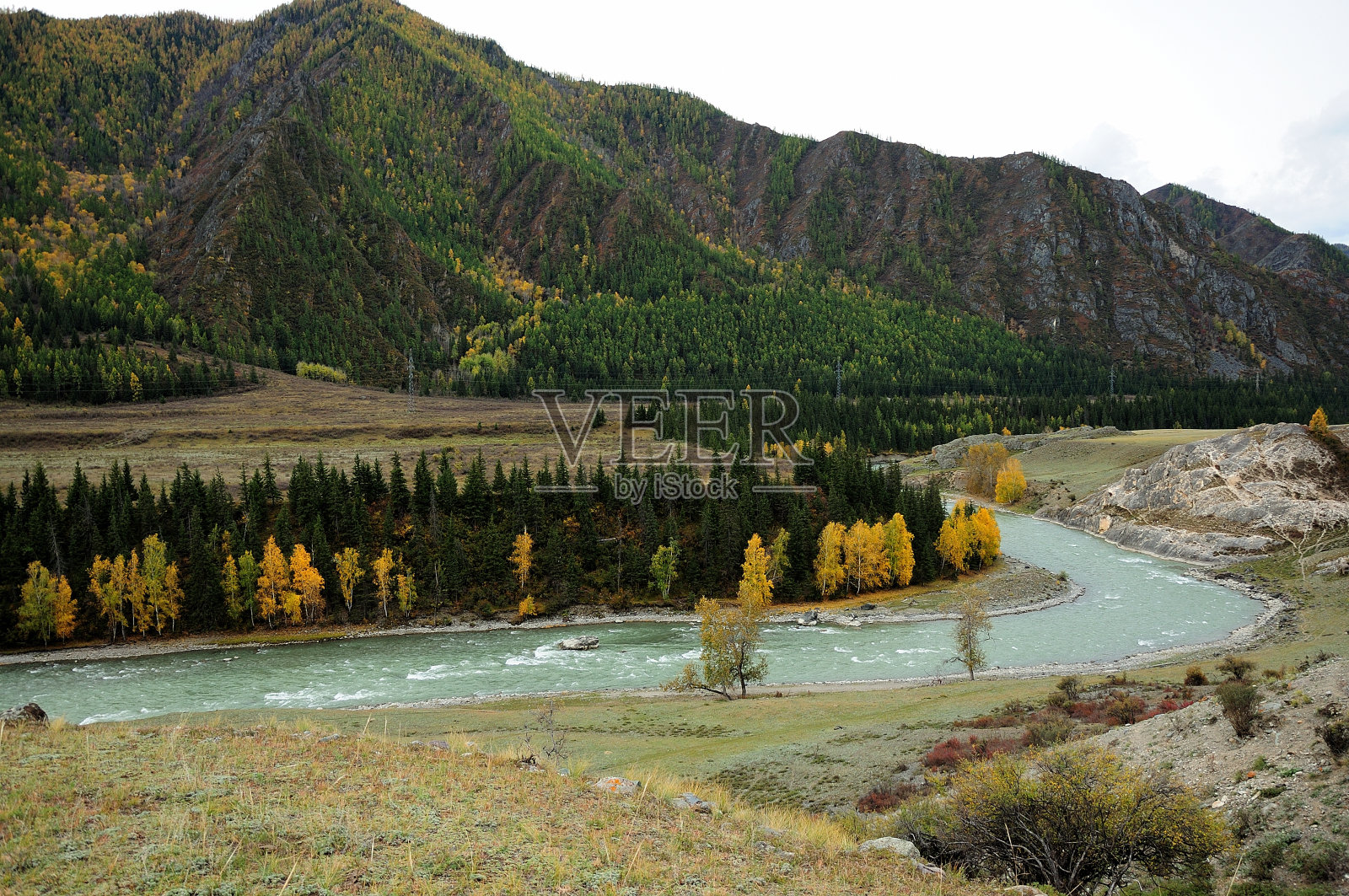 蜿蜒的河床，一条美丽的河流，流过高山脚下的秋天山谷。照片摄影图片