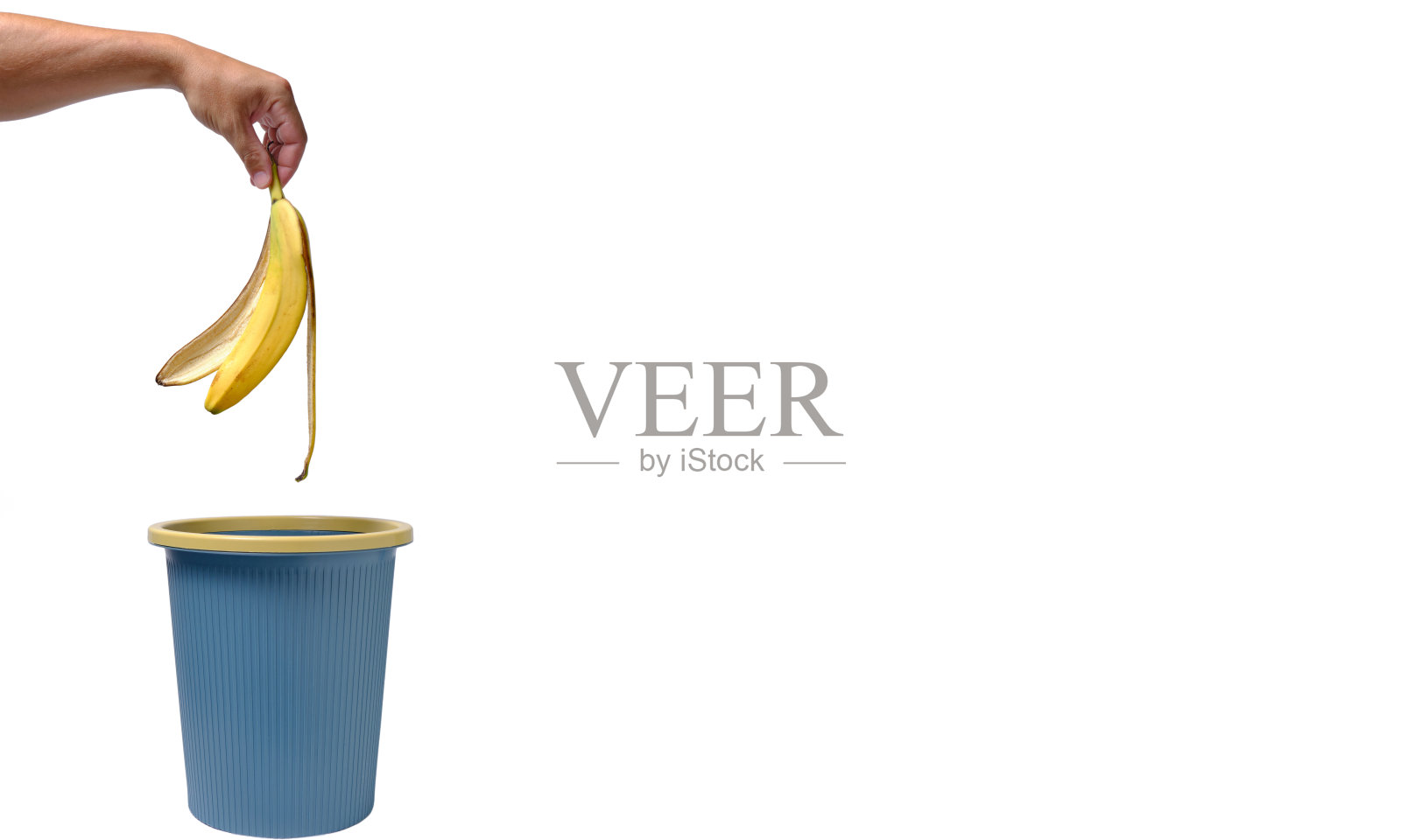 在一个男人的手里，香蕉皮被扔进了垃圾桶。食物浪费。照片摄影图片