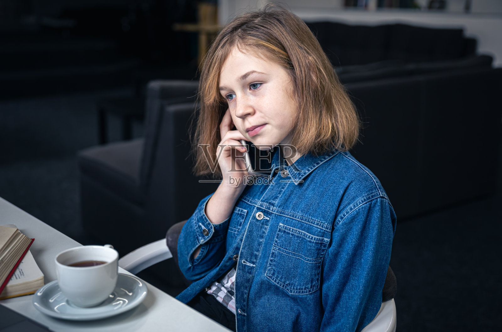 小女孩一边喝茶一边讲电话。照片摄影图片