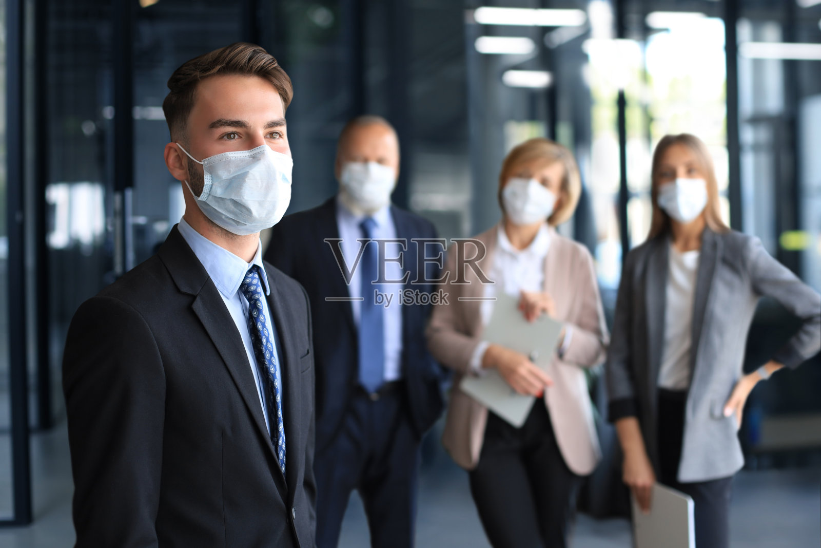 戴着医用口罩的商人和他的同事在办公室里。照片摄影图片