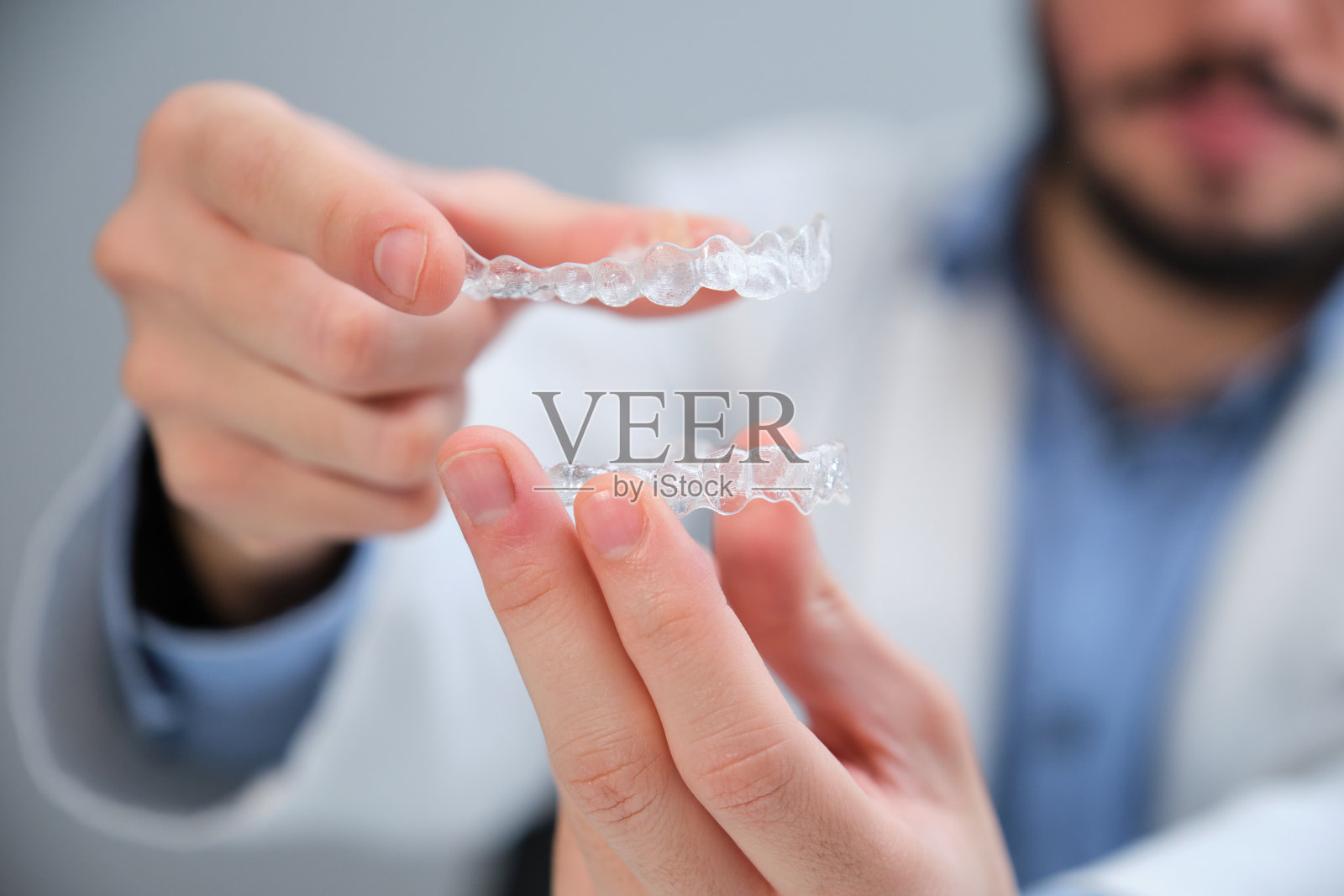 无法辨认的正牙医生拿着训练器牙齿矫正器。照片摄影图片