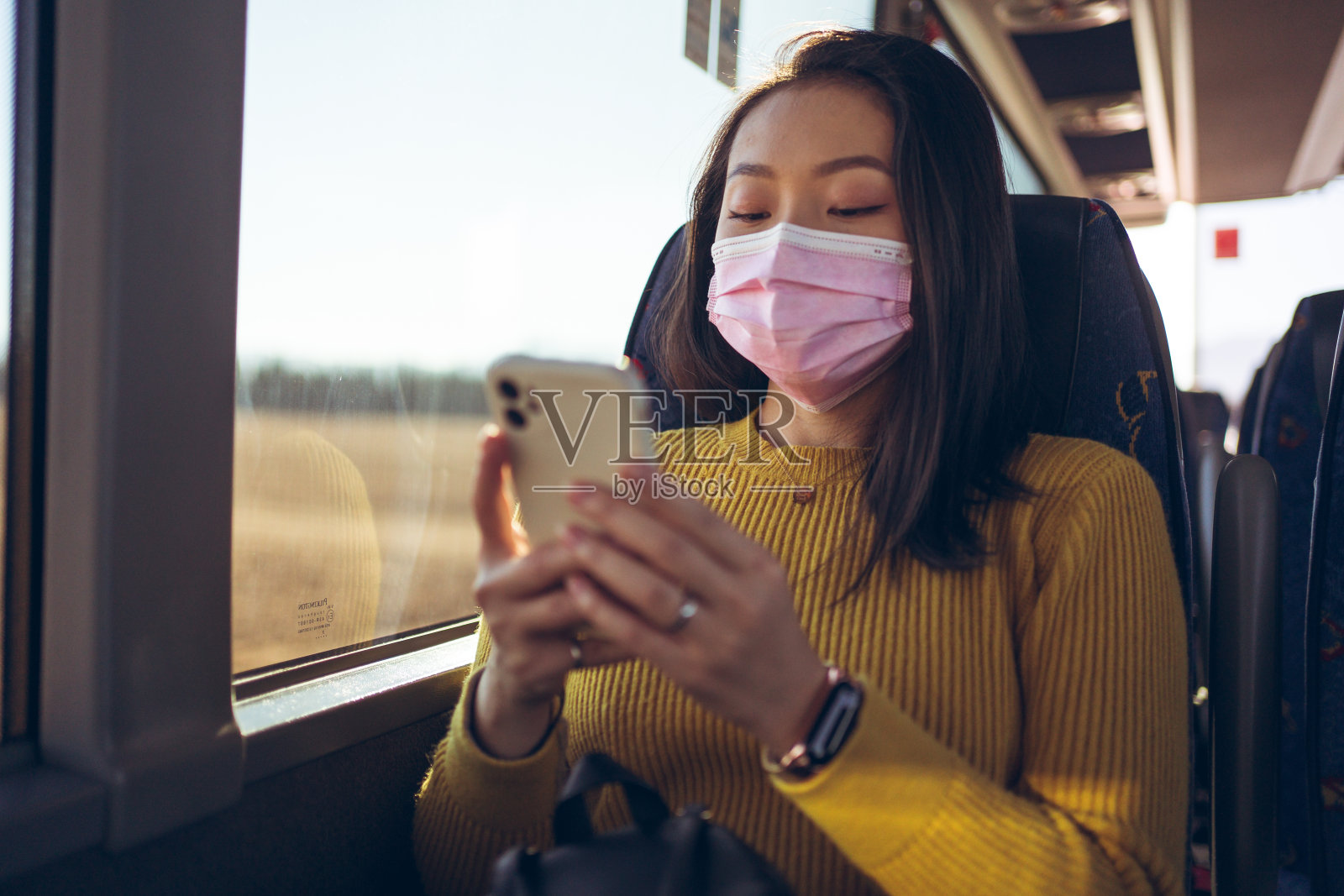 年轻的亚洲美女，戴着粉色口罩，乘坐空巴士，使用智能手机照片摄影图片