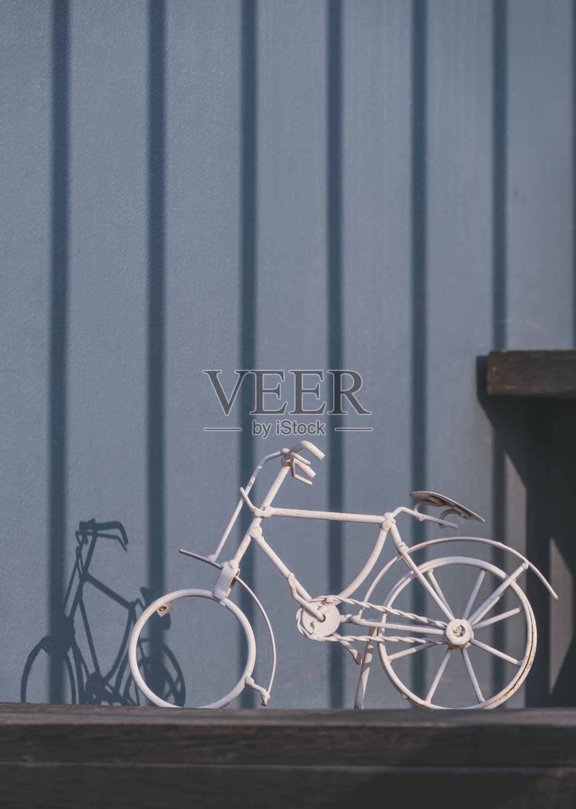 灯光和阴影在旧的老式白色微型自行车模型在木架上与灰色墙壁背景在最小的风格照片摄影图片