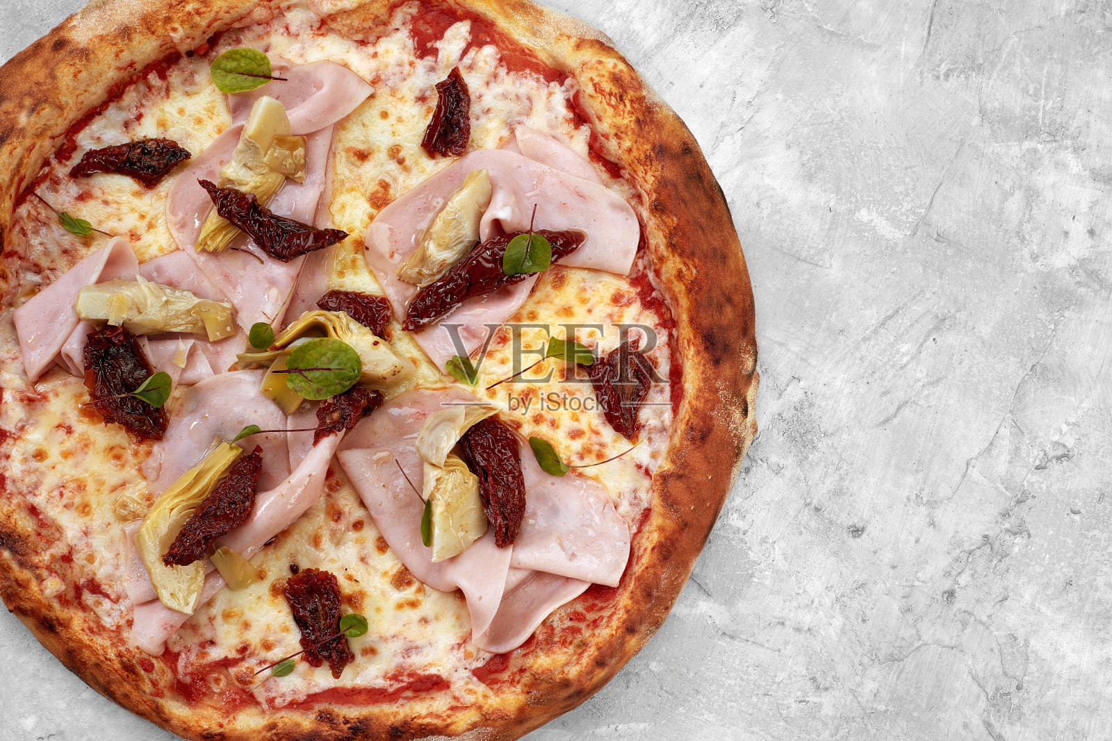 灰色的桌子上放着小牛肉、火腿、奶酪和西红柿干的披萨照片摄影图片