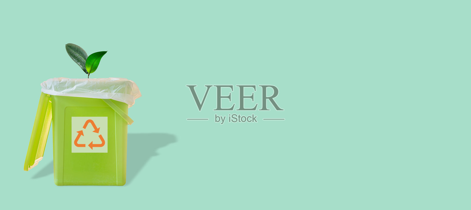 横幅与一个绿色的垃圾垃圾桶与袋子里面和生长一棵植物树和它的影子和回收符号在蓝绿色固体背景与复制空间。废物回收利用的概念。照片摄影图片