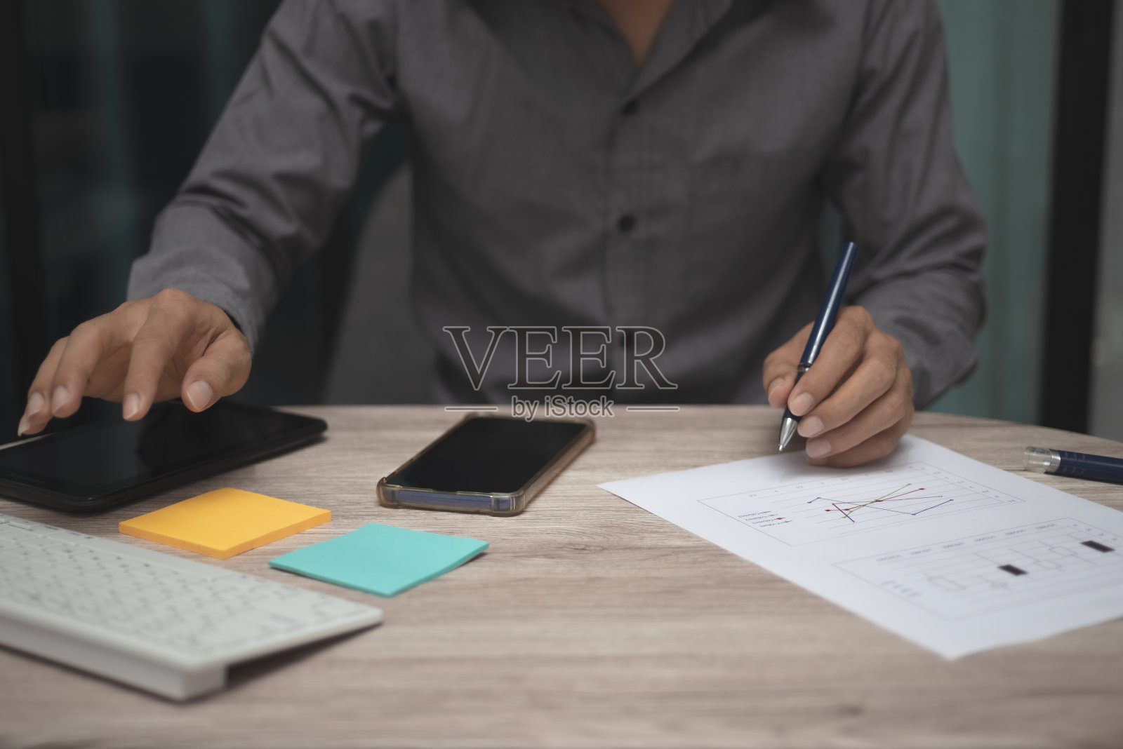 在办公室的桌子上工作的商人。人手用笔指着商业图或图表，用键盘、智能手机和平板电脑分析数据和策略，为投资成功目标。照片摄影图片