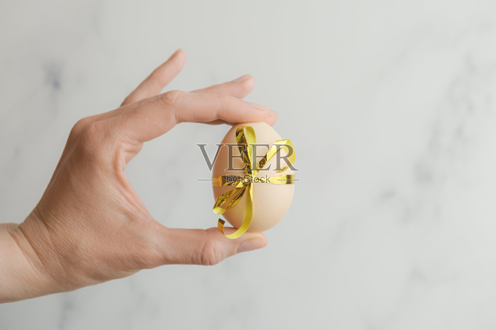 女性手拿着一个用节日彩带系在抽象灰色背景上的大鸡蛋照片摄影图片