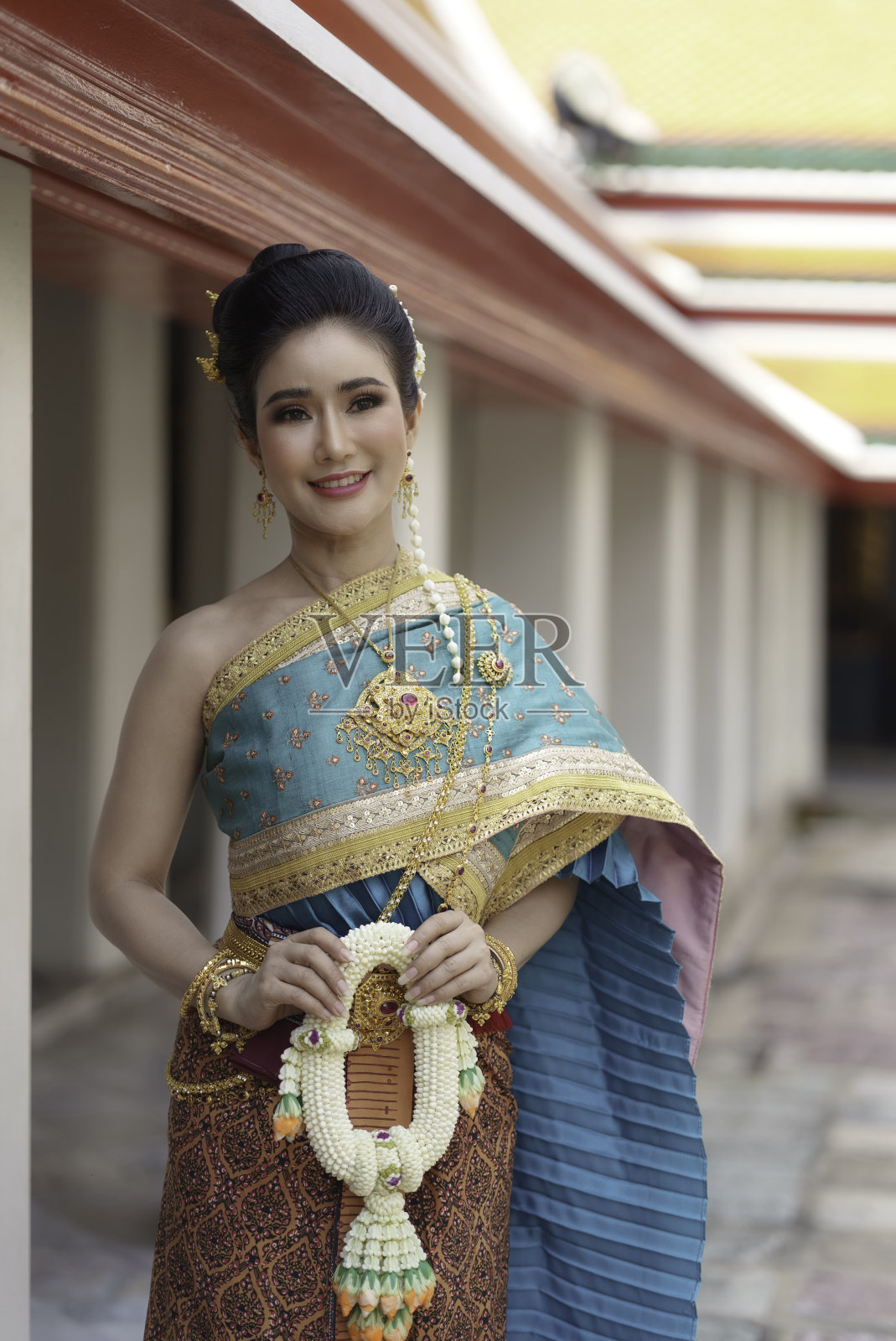 在泰国人民重要的宗教节日里，身着泰国民族服装、面带微笑的亚洲妇女在寺庙里用花环拜佛。照片摄影图片