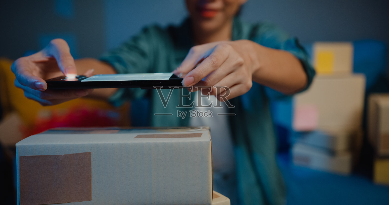 年轻的亚洲女售货员在网上商店使用智能手机上的手机应用程序，晚上检查快递到客户家里的包裹。照片摄影图片