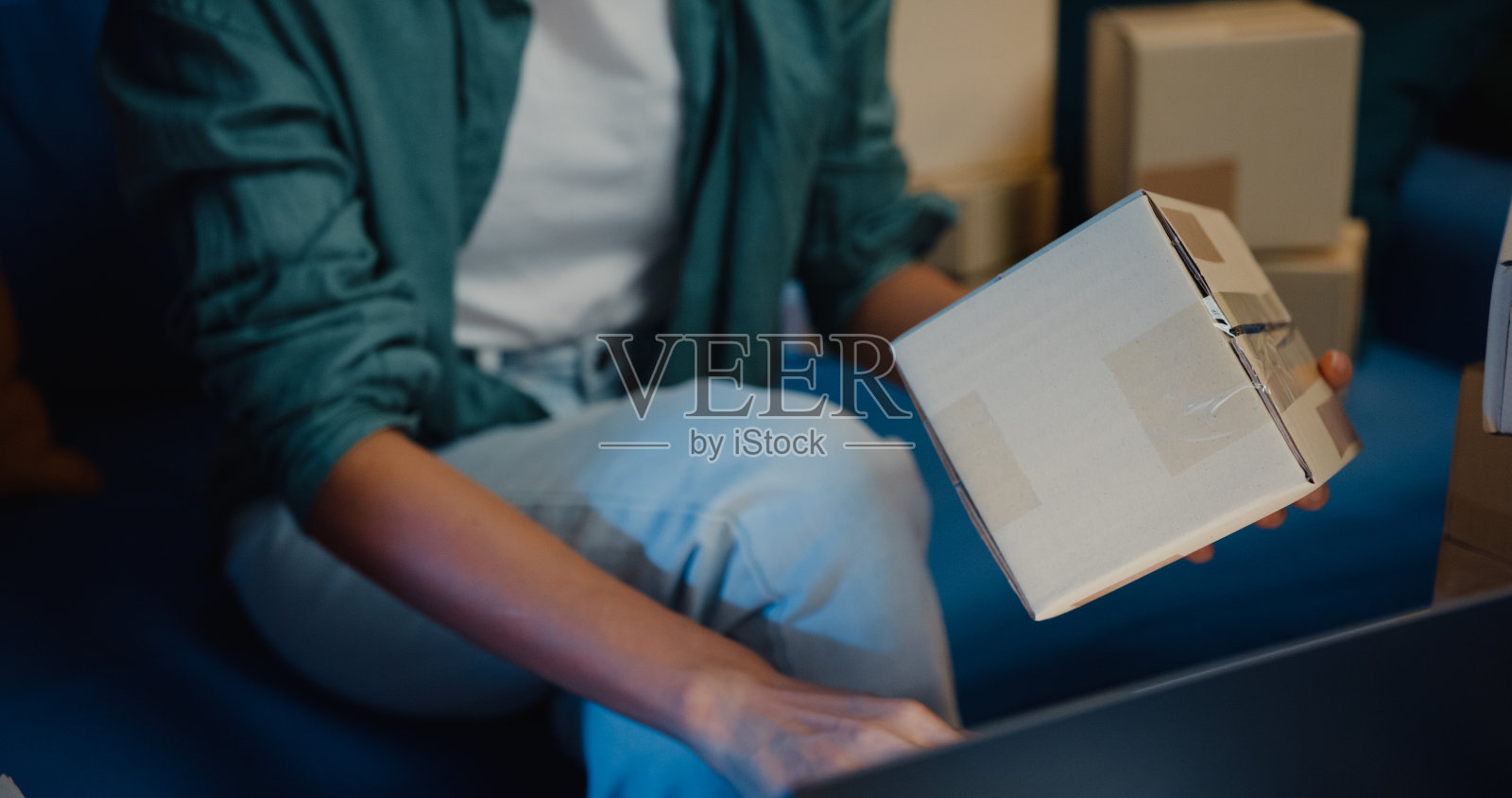 接近年轻的亚洲女售货员使用笔记本电脑在线商店准备运送到客户在家里晚上的包裹。照片摄影图片