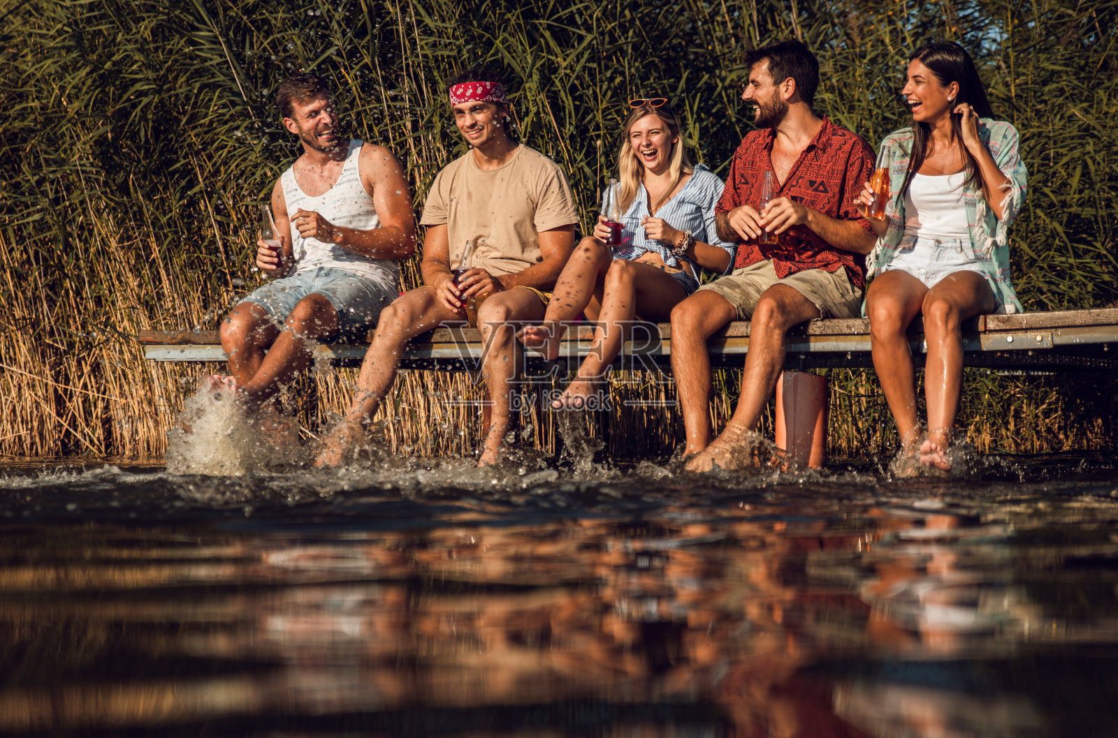 一群朋友坐在码头边，享受着夏日的湖面。照片摄影图片