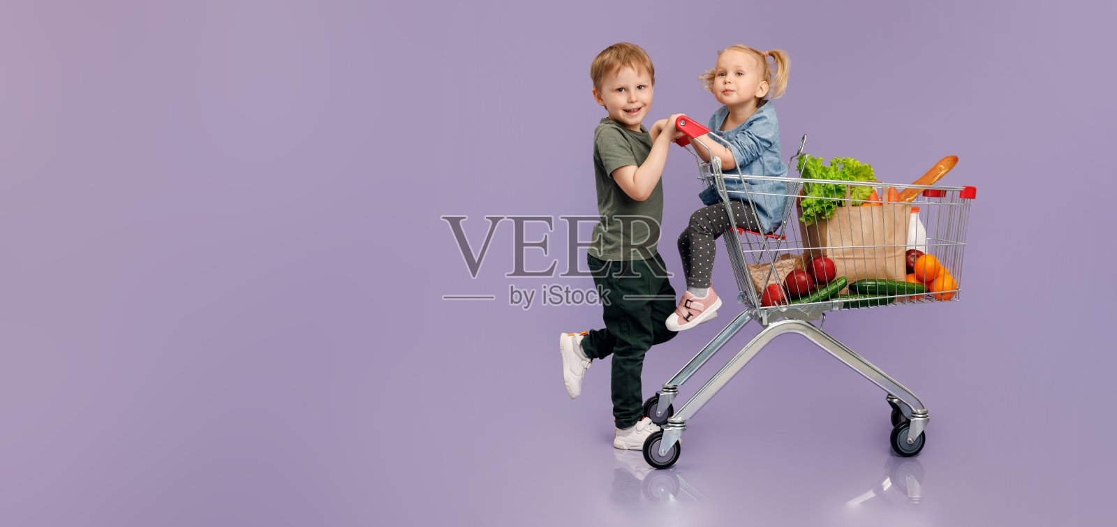 一个小男孩推着一个小女孩在购物车里。孤立的概念形象。“n照片摄影图片