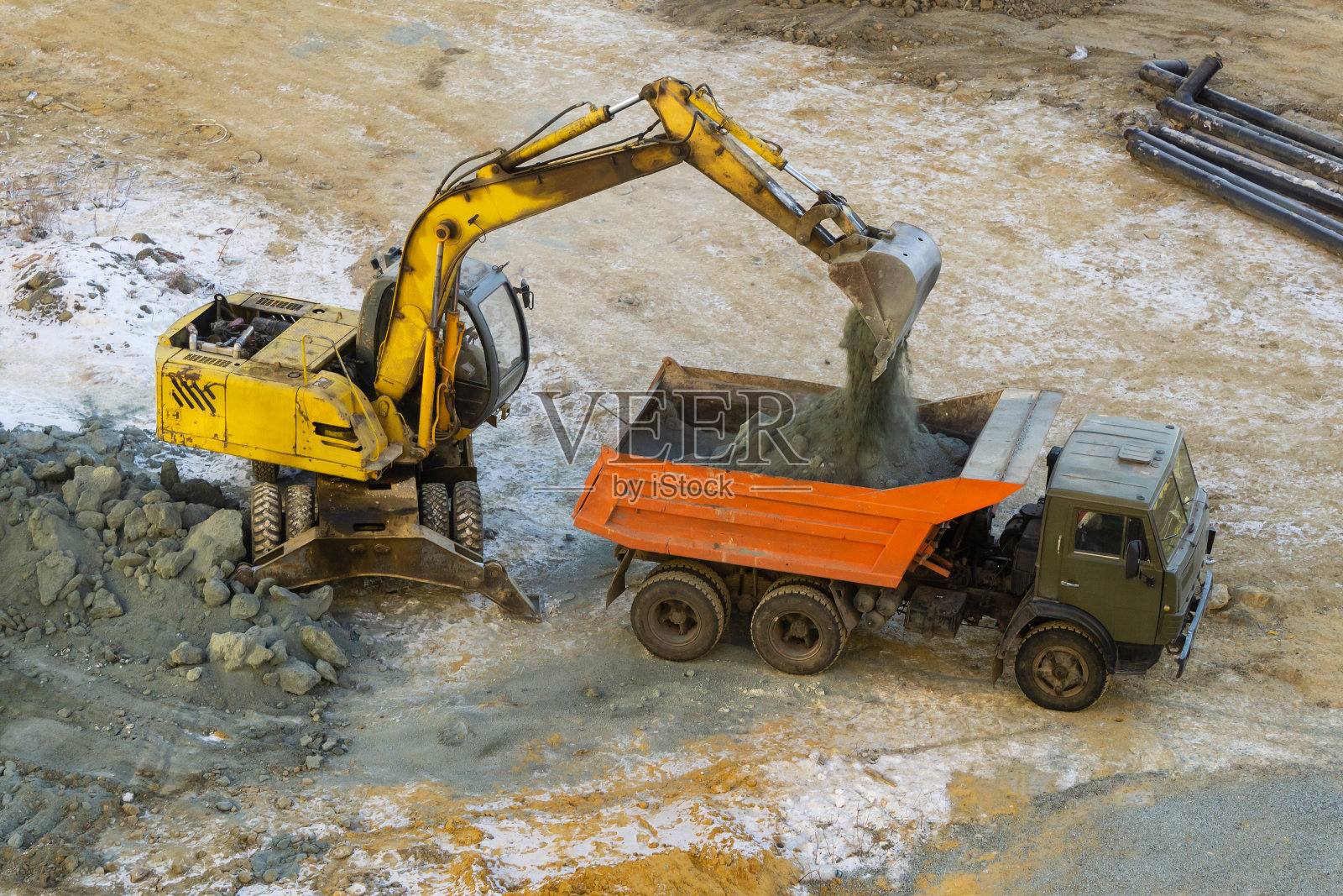 用挖掘机把碎石装到卡车上。挖掘机铲斗将砾石卸到卡车后面，俯视图。冬季施工现场。照片摄影图片