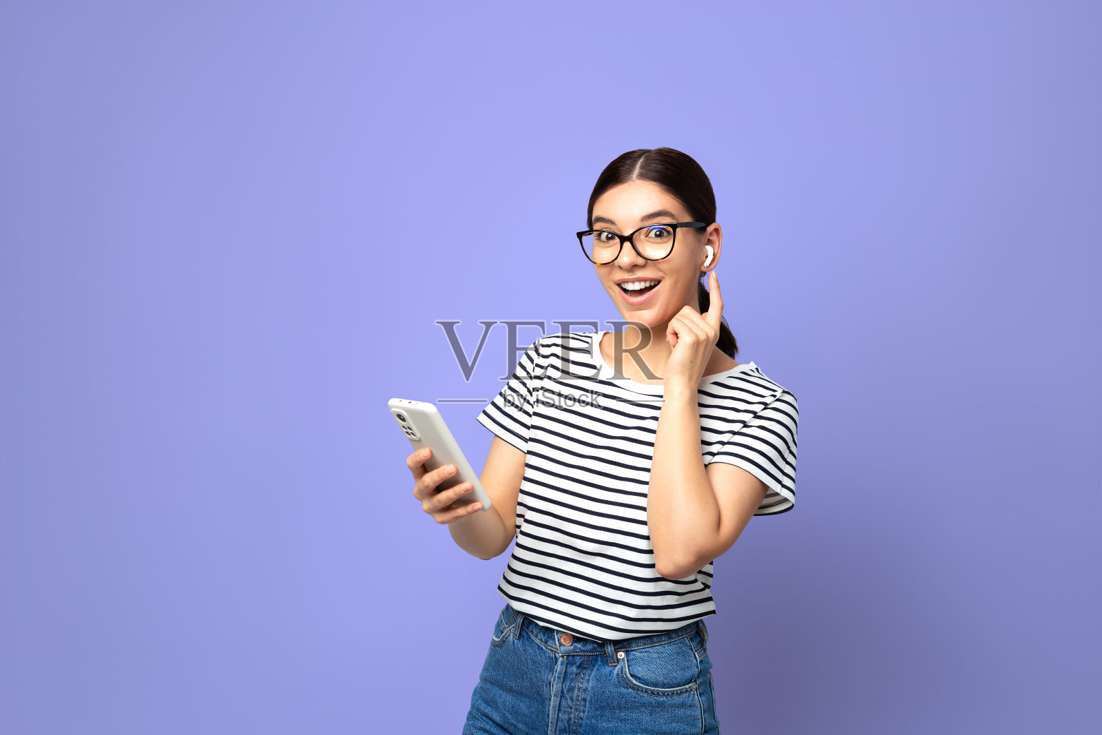 有吸引力的深褐色条纹t恤使用小的白色无线耳机在紫色非常接近的颜色背景照片摄影图片