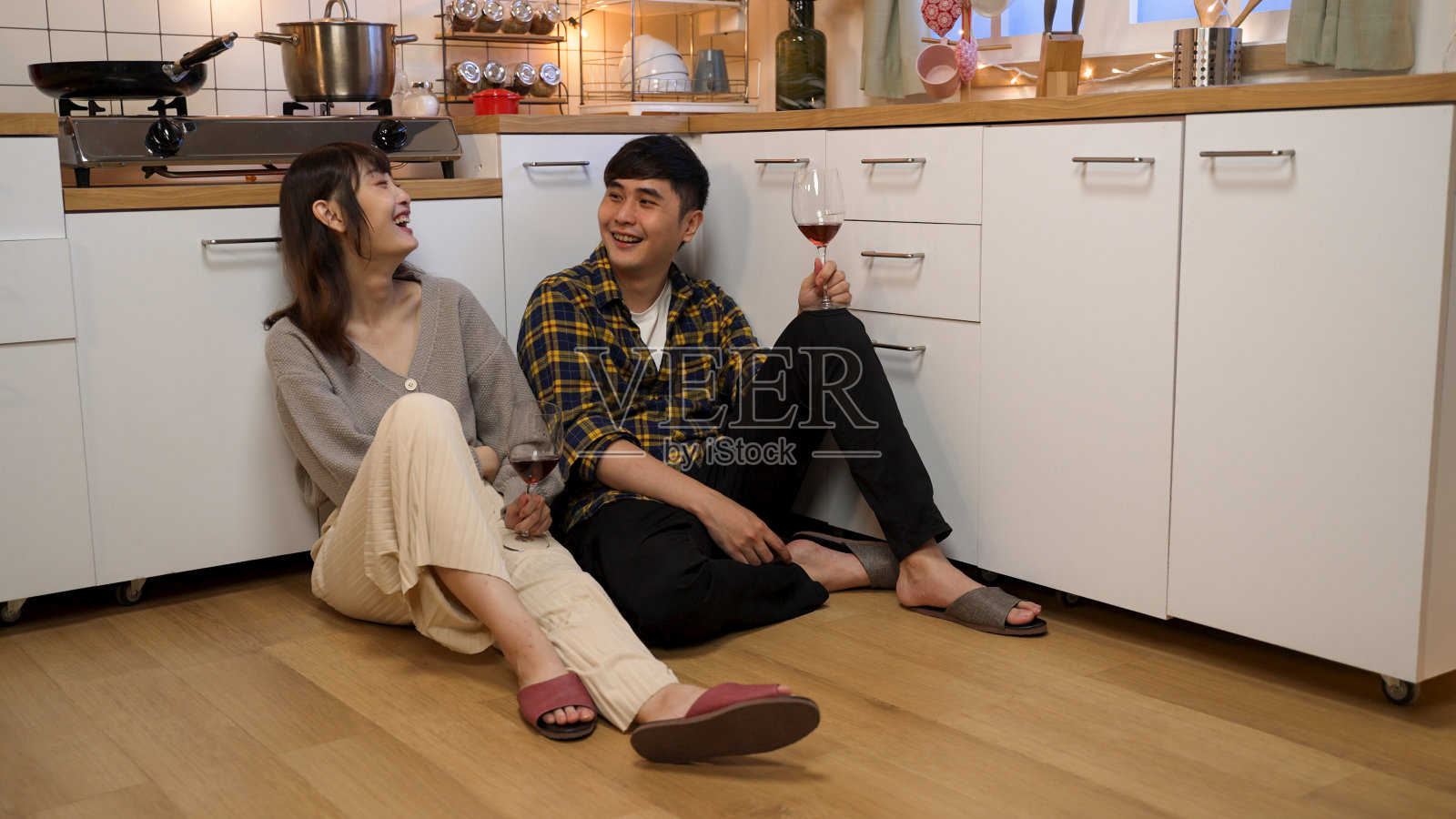 微笑的亚洲夫妇一起度过情人节之夜坐在地板上，享受从厨房里的玻璃杯里的香槟照片摄影图片