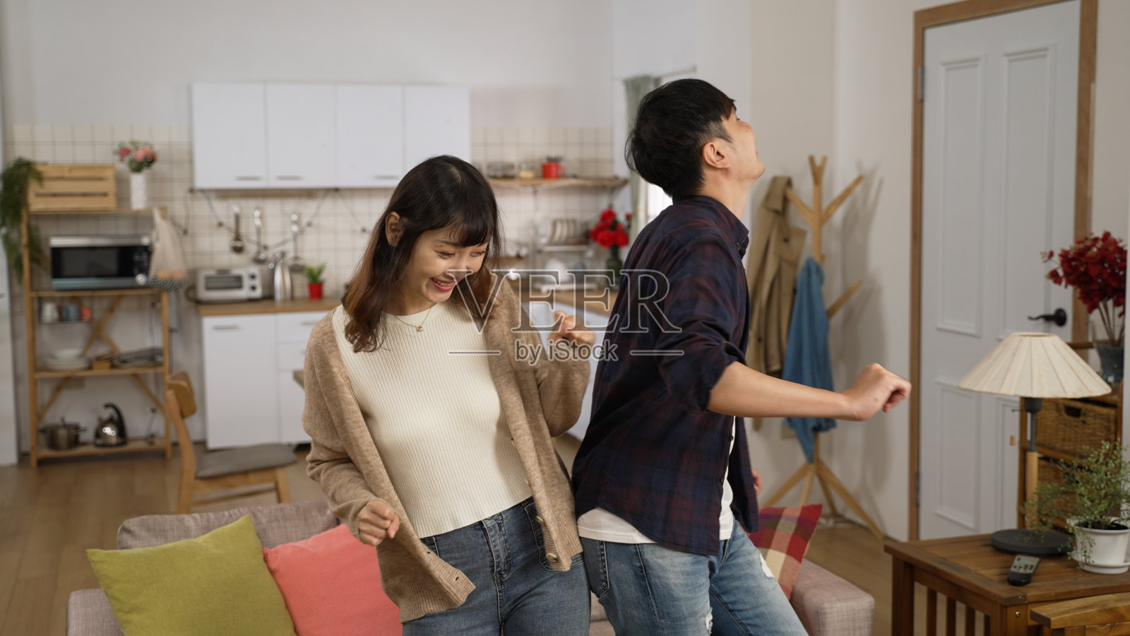 喜气洋洋的亚洲夫妇在家里的客厅里一起跳舞。丈夫用滑稽的舞步轻轻触碰妻子的身体。照片摄影图片