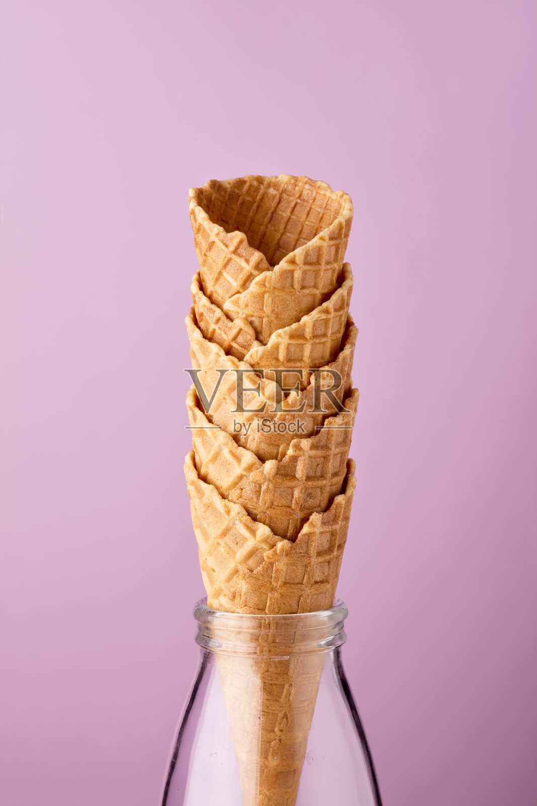 空的冰淇淋甜筒在玻璃牛奶瓶对紫色的背景。照片摄影图片