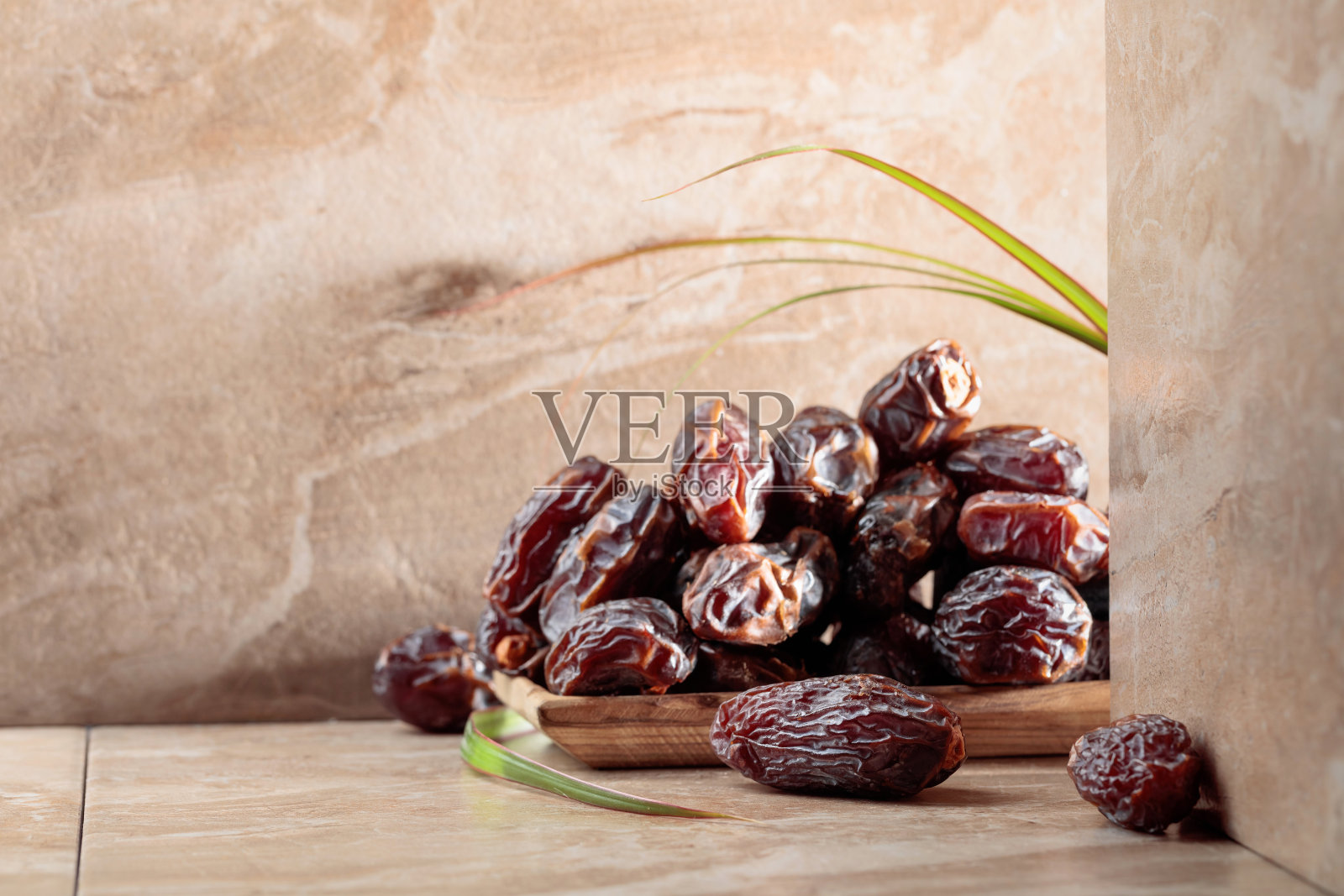 米色陶瓷桌子上的木制盘子里放着椰枣。照片摄影图片