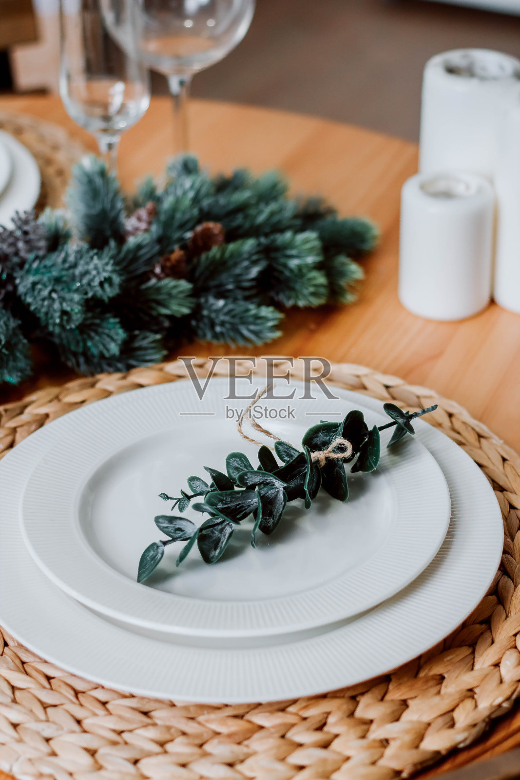 有桉树叶小枝的盘子。为圣诞节和新年装饰的圆桌。圣诞树的小树枝放在桌子上。盘子和酒杯放在桌子上。厨房用具和背景上的鲜花。圣诞节的内容。照片摄影图片