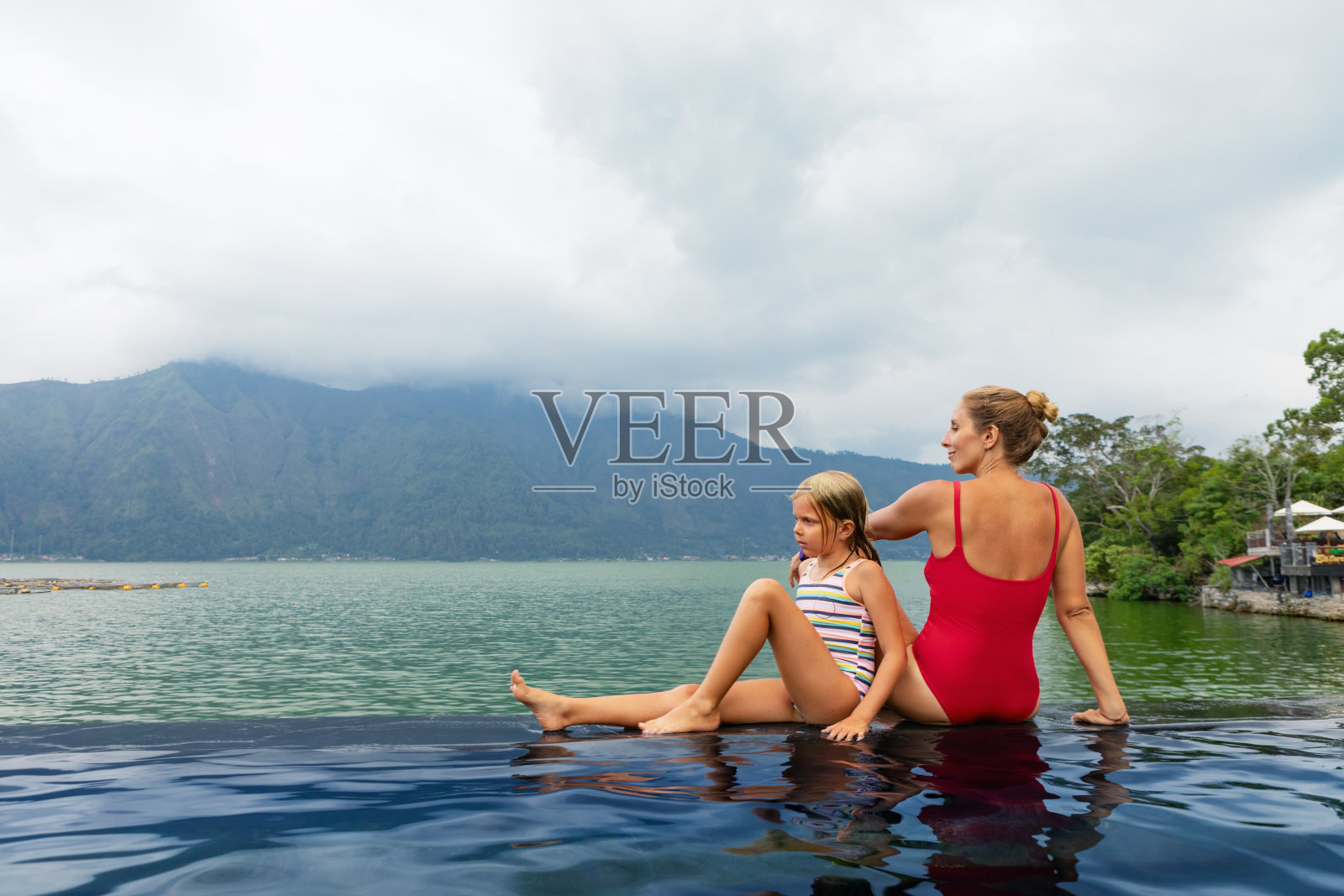 幸福的家庭在巴图尔火山温泉温泉。去巴厘岛的金塔马尼旅游。母亲和孩子在泳池里享受着湖景。健康的生活方式，暑假与孩子们一起进行娱乐活动照片摄影图片