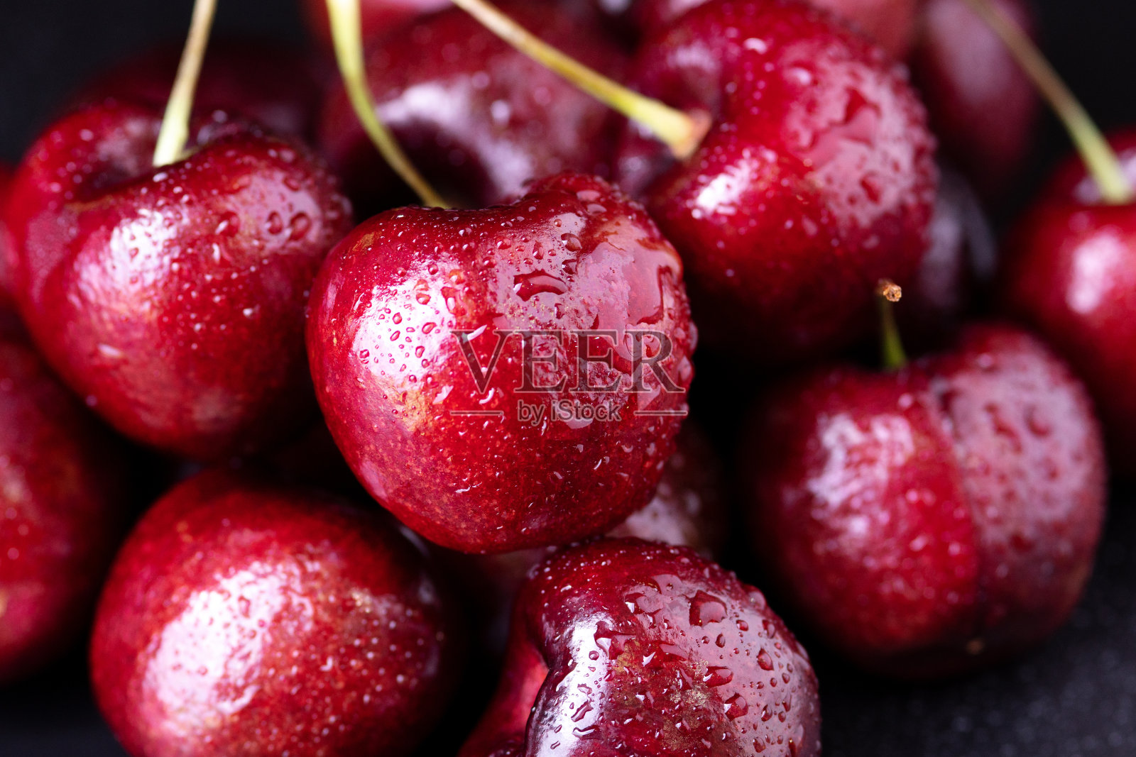 鲜樱桃和水滴在黑色的桌子上。照片摄影图片