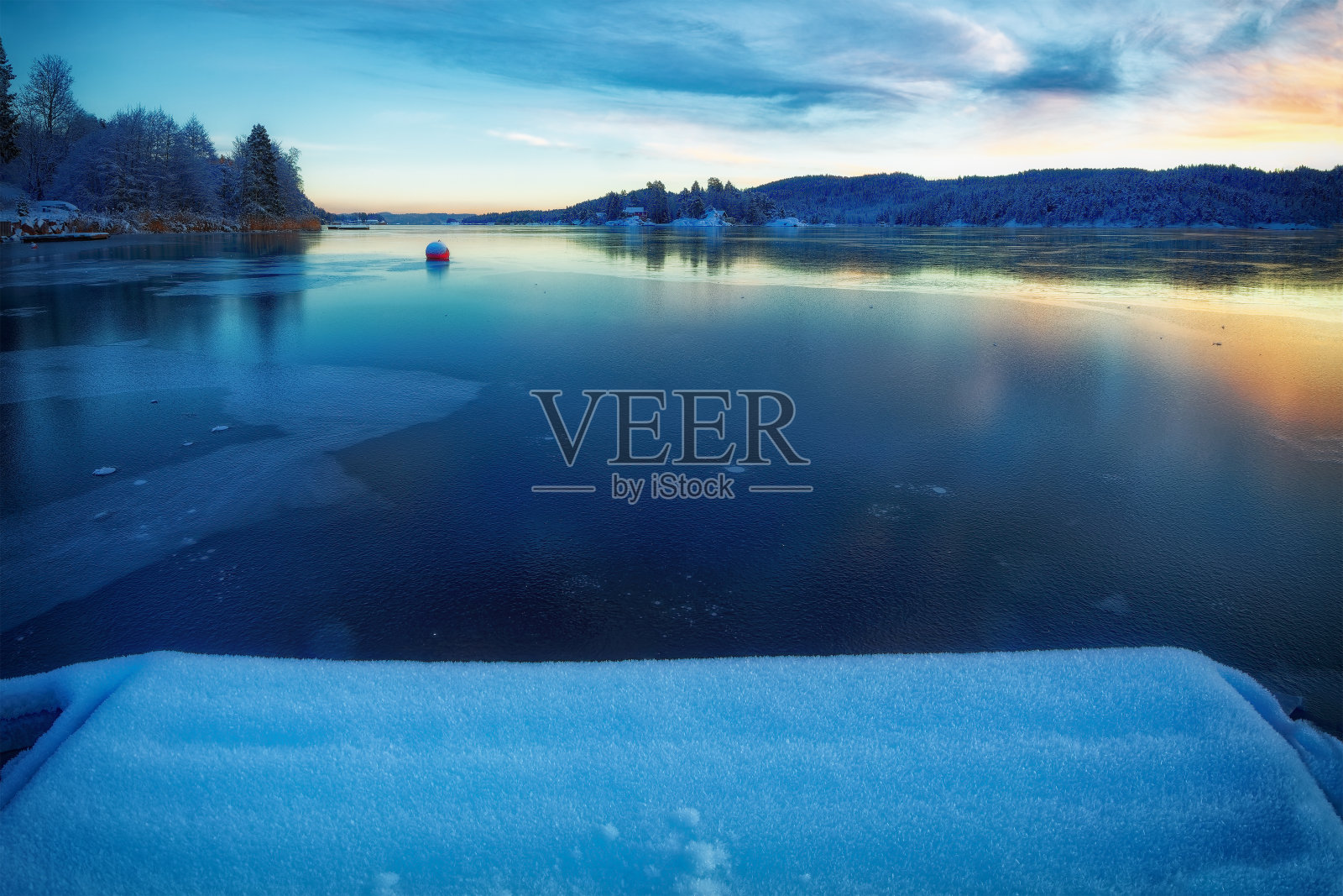 峡湾被冰覆盖，五颜六色的天空在冰中反射。冰雪覆盖的码头在前景。岛屿、小屋、大海、白雪皑皑的岩石、蔚蓝的天空、落日的倒影。挪威的黄昏。照片摄影图片