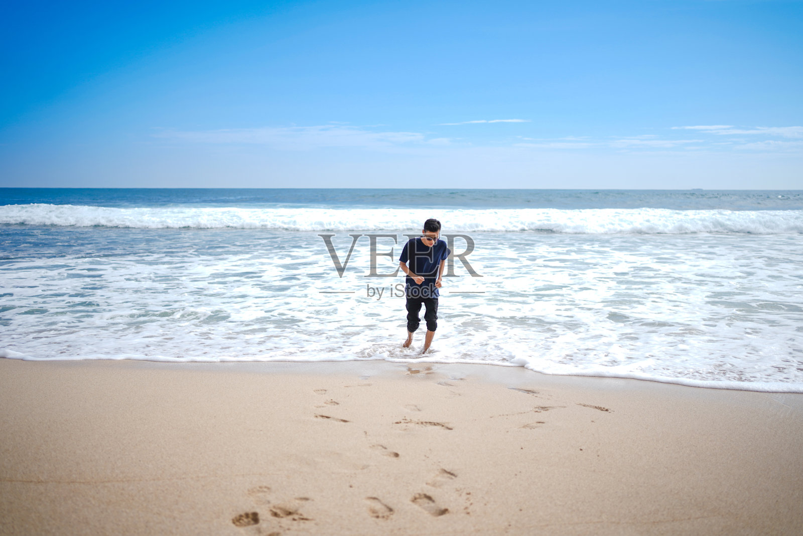 一个穿着蓝色衬衫的男人，被海浪追逐着。这个海滩看起来很漂亮，干净和白色的沙子照片摄影图片