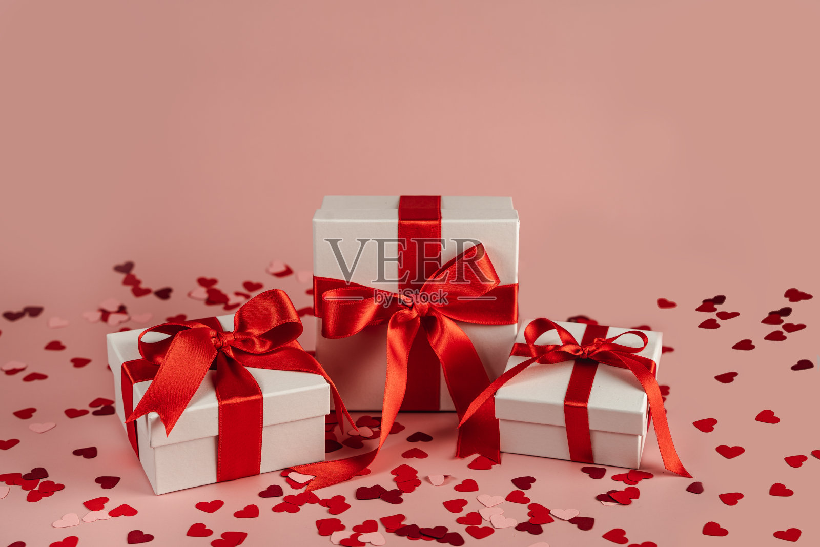 玫瑰背景上的红色蝴蝶结与心形纸屑礼物。平的风格。情人节的概念。圣情人节照片摄影图片