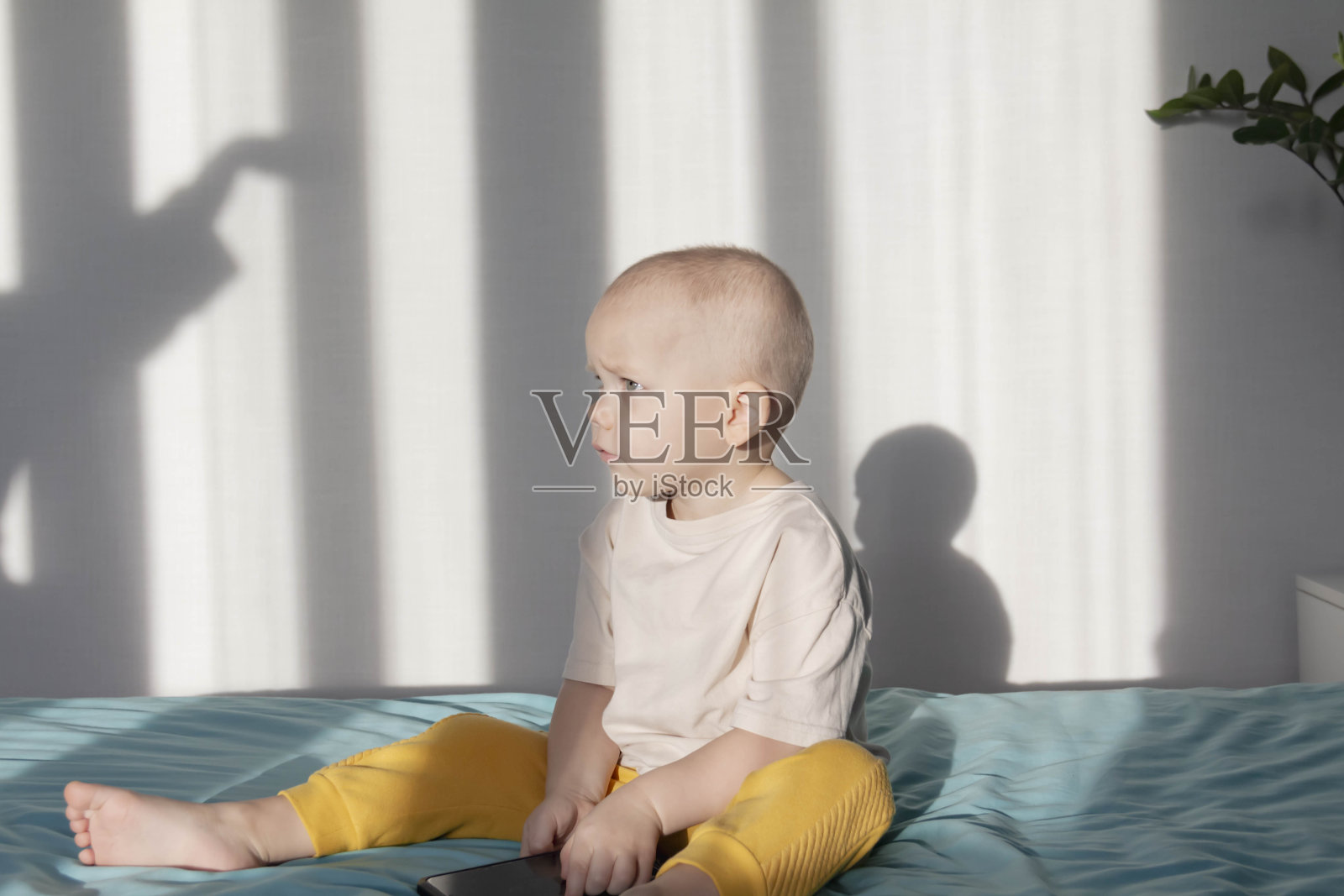 一个小男孩坐在床上的蓝色毯子上玩一部现代手机。照片摄影图片