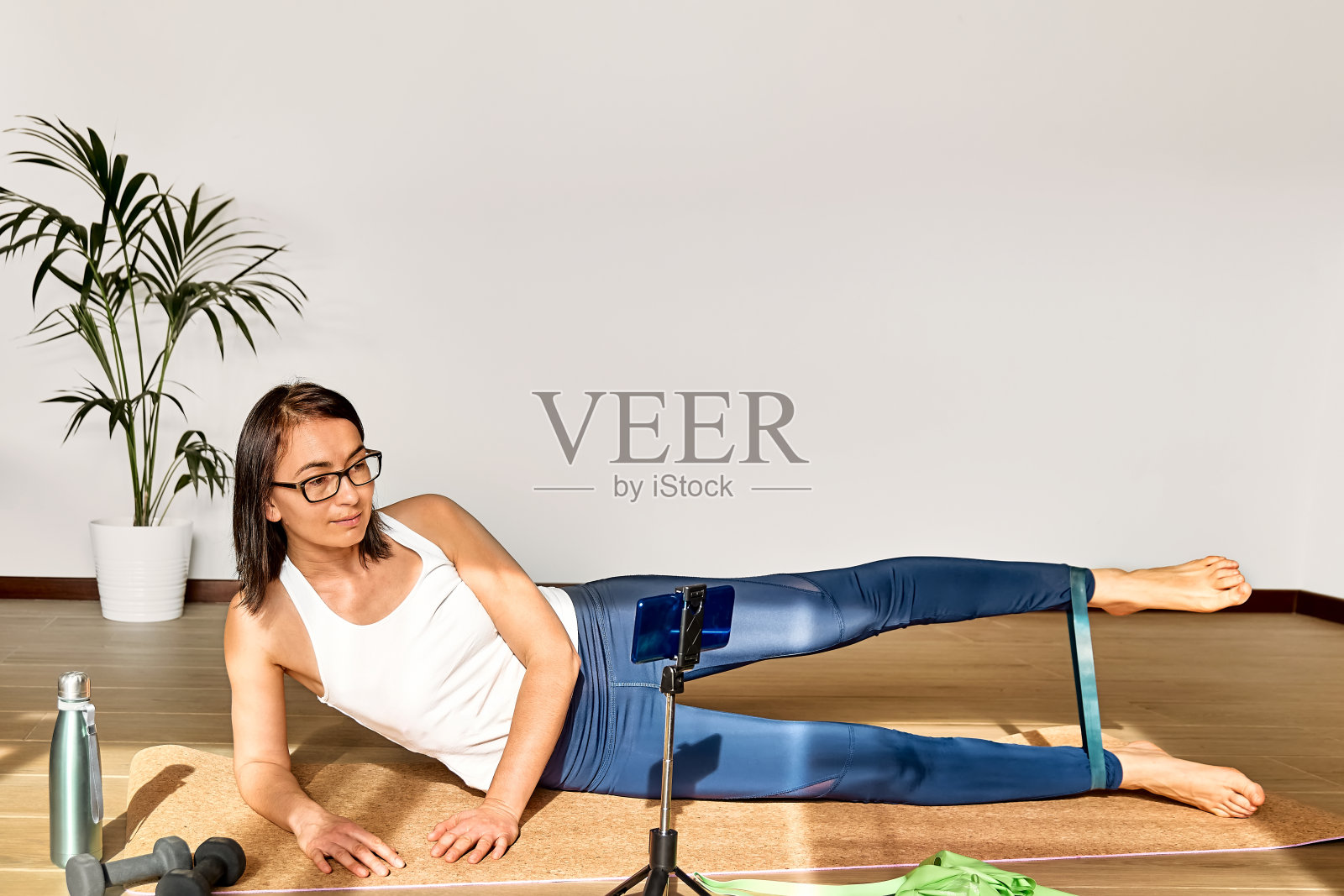 运动女性在家里用阻力带进行健身训练，通过她的智能手机进行在线锻炼。健康的生活方式。照片摄影图片