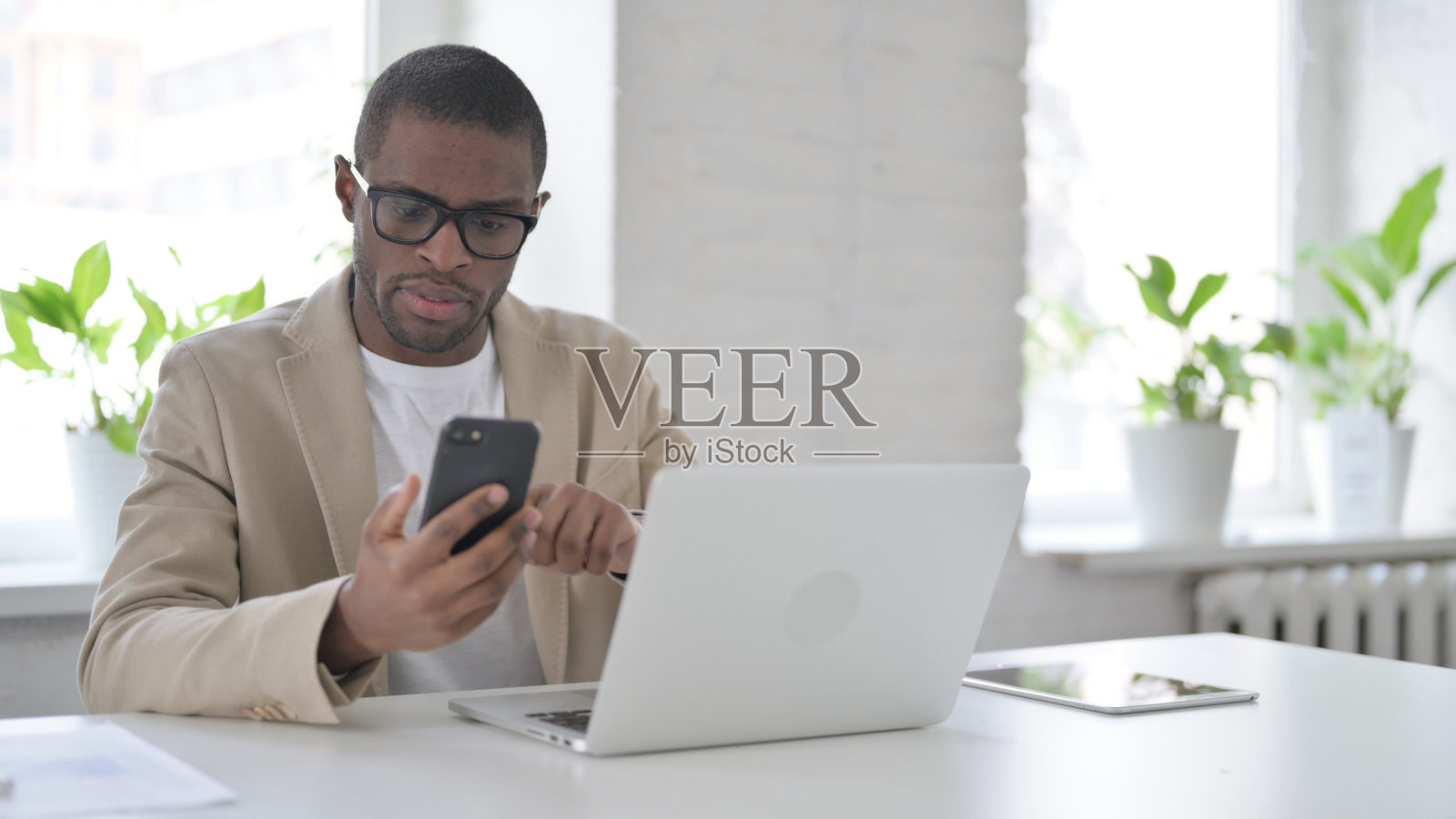 非洲人在办公室使用笔记本电脑时使用智能手机照片摄影图片