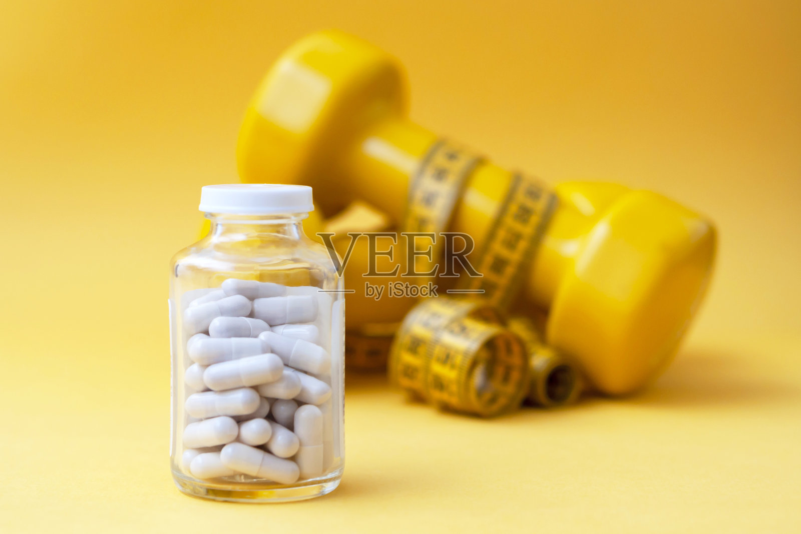 药丸胶囊在一个玻璃罐里，有哑铃和一个厘米的磁带作为背景。减肥的概念，运动健身，燃脂，维生素，运动营养。照片摄影图片