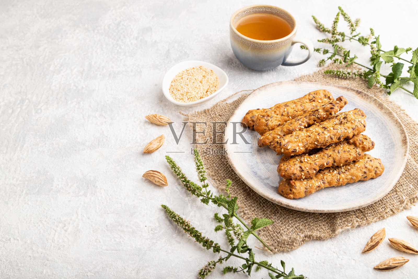 碎饼干与海葵和杏仁在陶瓷盘子与一杯绿茶灰色混凝土背景。侧视图，复制空间。照片摄影图片