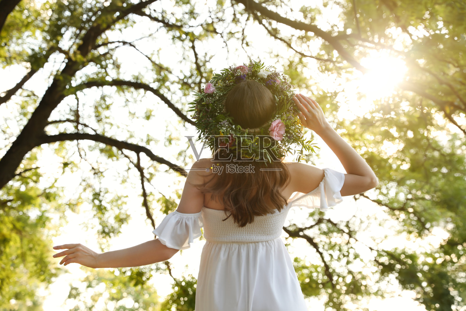 在阳光明媚的日子里，年轻女子戴着由美丽的花朵制成的花环在户外，后视图照片摄影图片