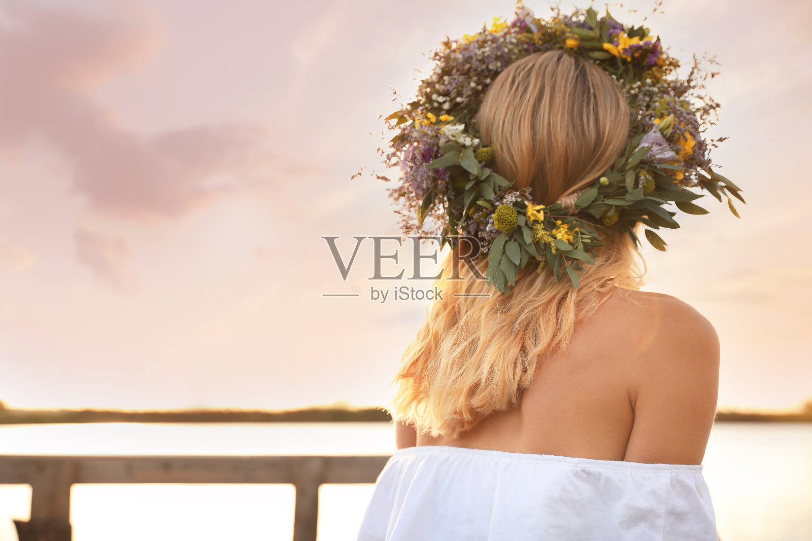 在阳光明媚的日子里，一个年轻女子戴着美丽的花冠站在河边照片摄影图片