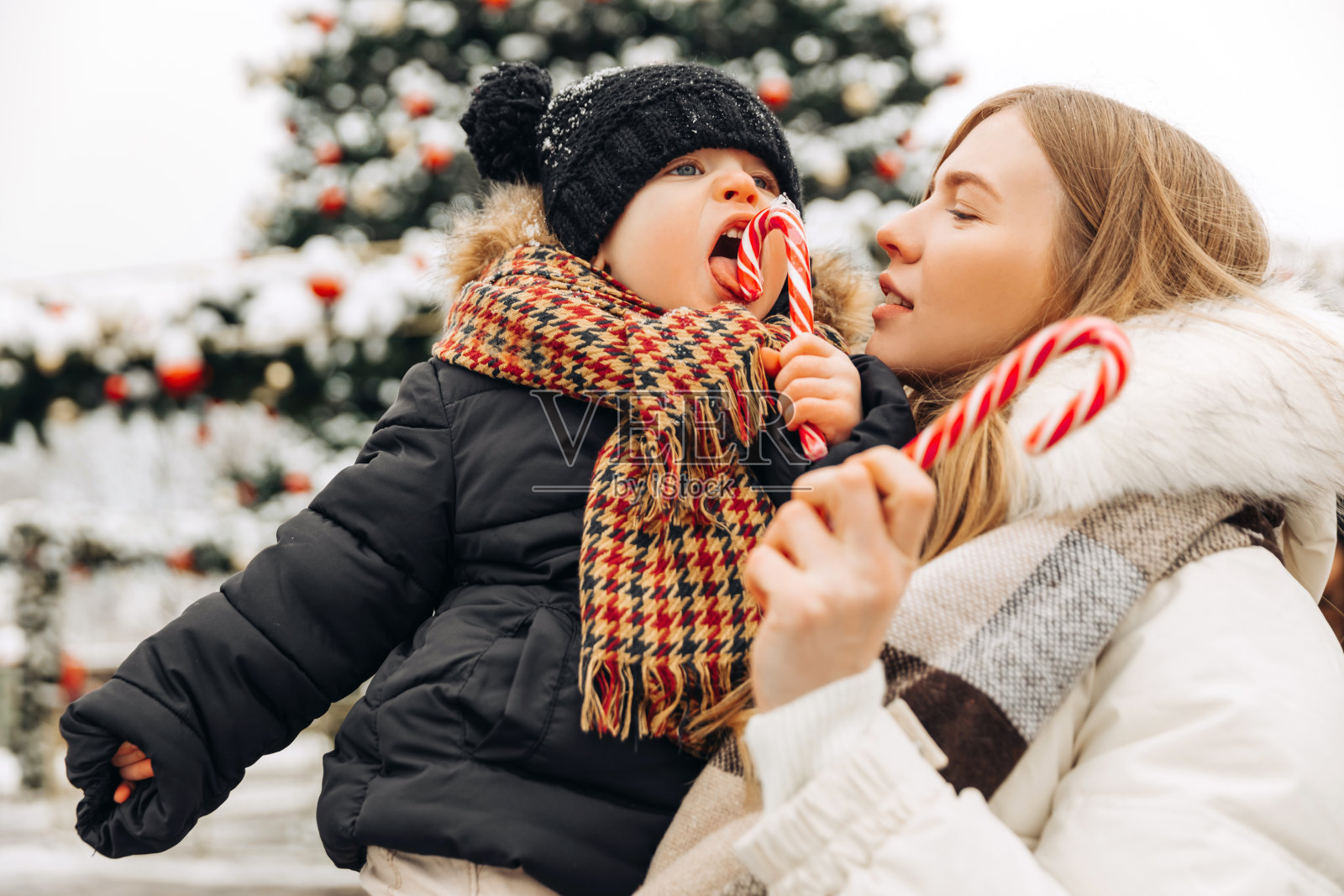 快乐的妈妈和孩子带着圣诞糖果，在圣诞集市上，幸福的家庭在城市的背景上照片摄影图片