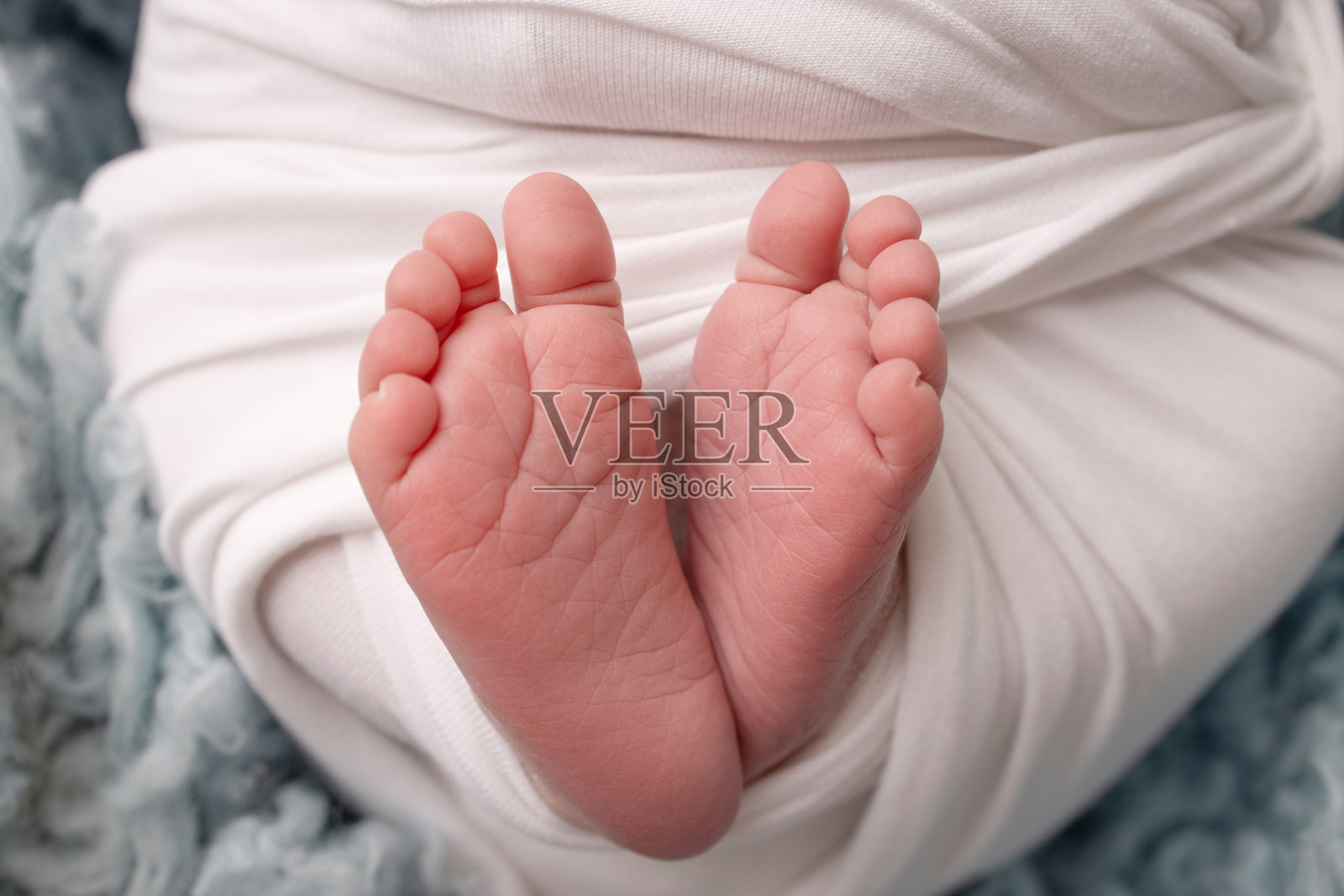 新生儿的小脚。在蓝色背景的白色毯子里，一个新生儿柔软的脚。新生儿的脚趾，脚跟和脚的特写。微距摄影工作室。女人的幸福。照片摄影图片