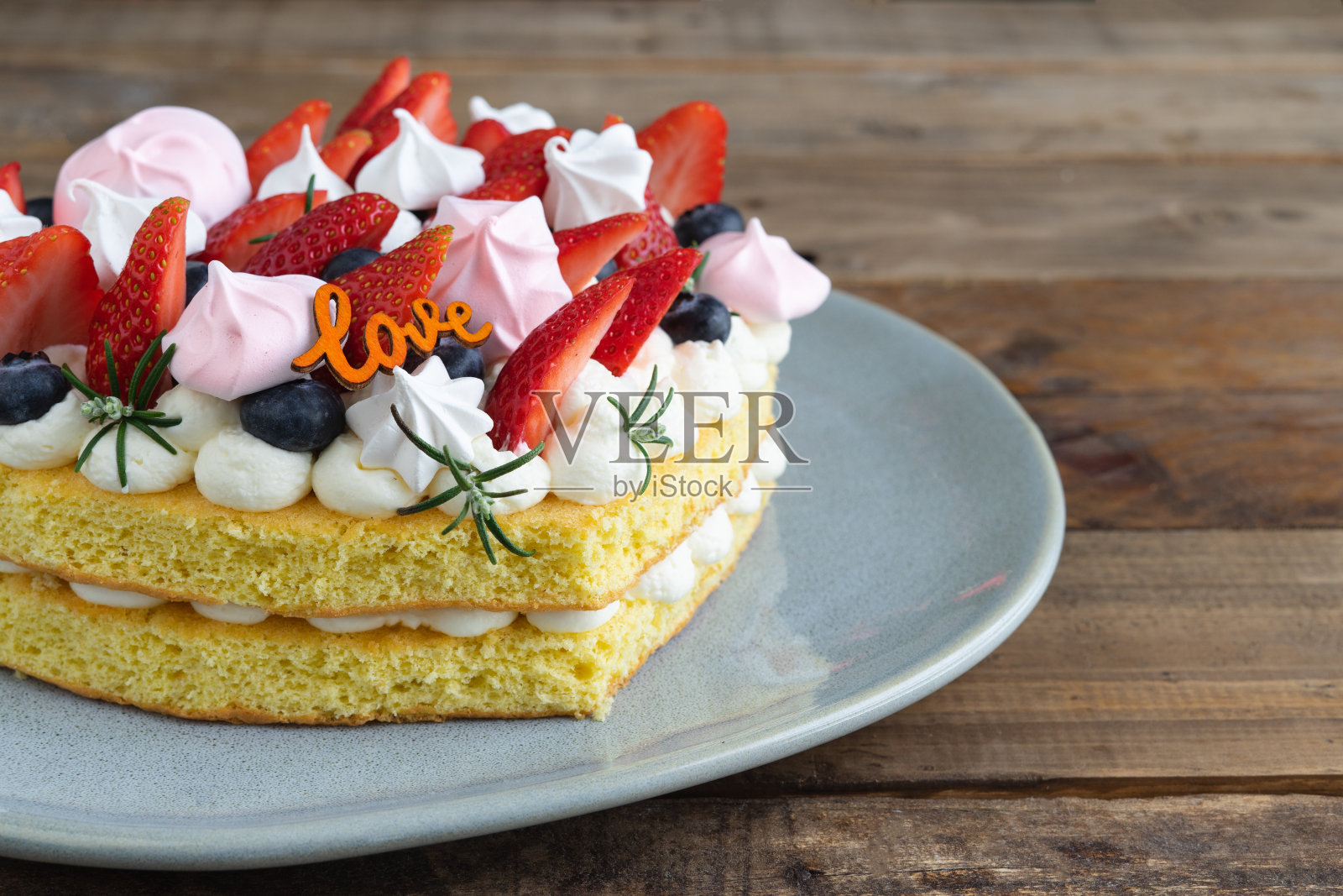 用红色水果和蛋白酥装饰的心形蛋糕。木基地。情人节。副本的空间。照片摄影图片