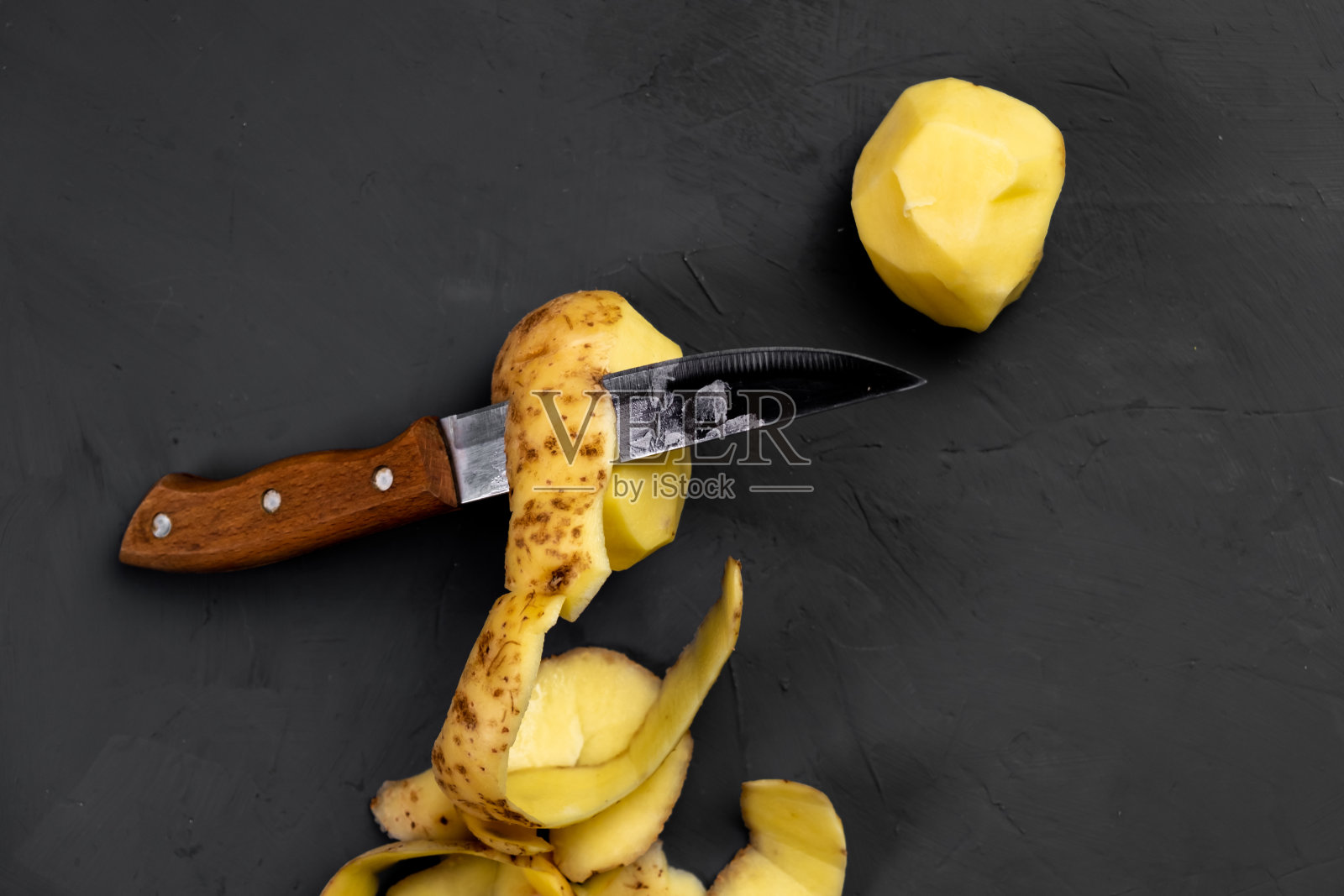 土豆和刀。土豆脱皮。黑暗的背景。准备煮土豆。照片摄影图片