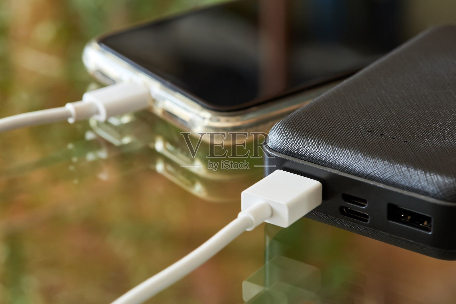 Power bank通过USB数据线在玻璃表面为智能手机充电。特写,有选择性的重点照片摄影图片