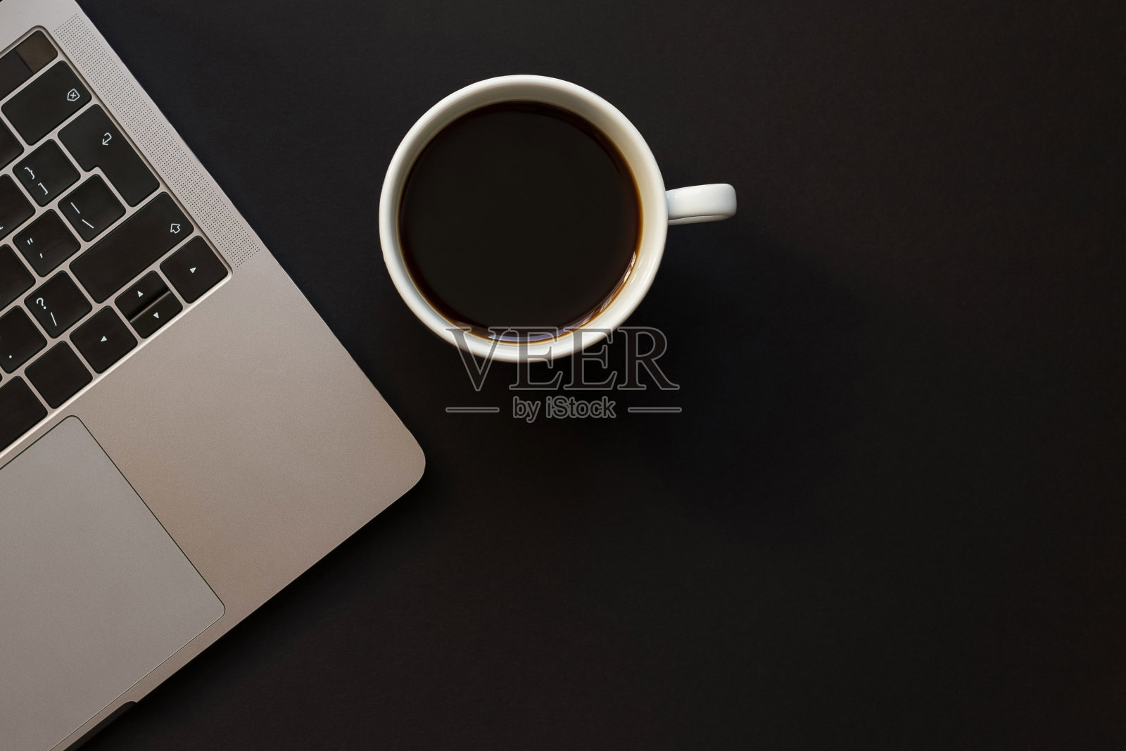 一张黑色的桌子，一台笔记本电脑和一杯咖啡。照片摄影图片