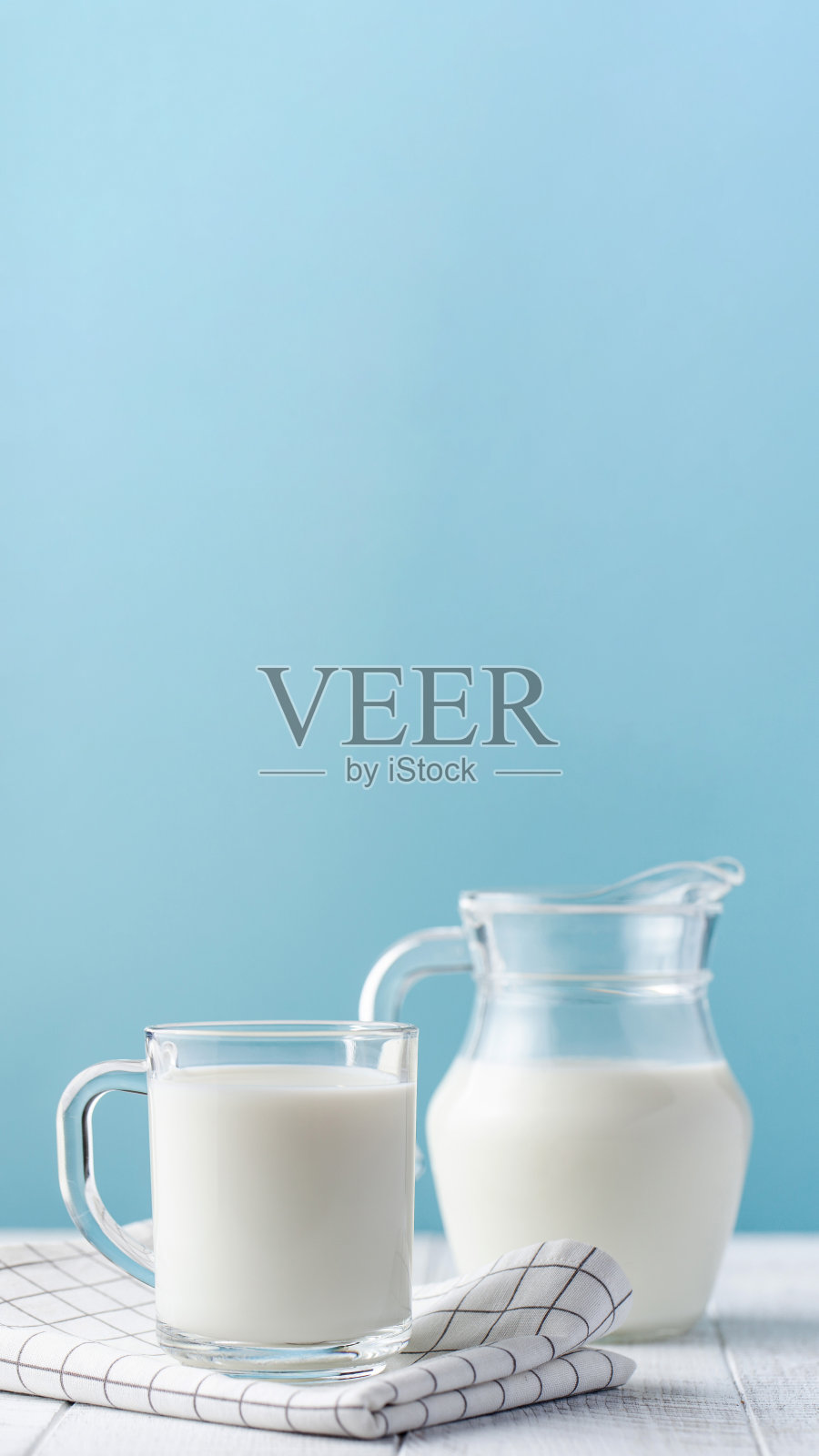 一壶和一杯鲜奶放在蓝色的背景上。照片摄影图片