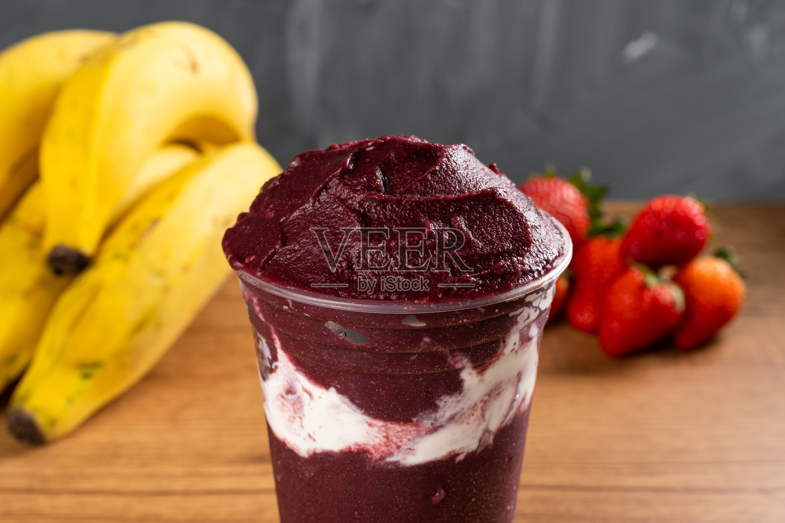 巴西冷冻Açai浆果冰沙在塑料杯炼乳。在一张木桌上，夏天的背景是灰色的水果。菜单和社交媒体的前视图照片摄影图片