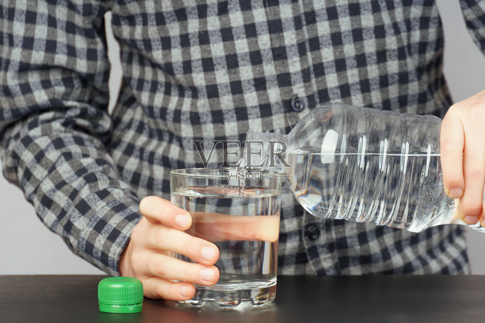 男孩把水从塑料瓶里倒进玻璃杯里。照片摄影图片