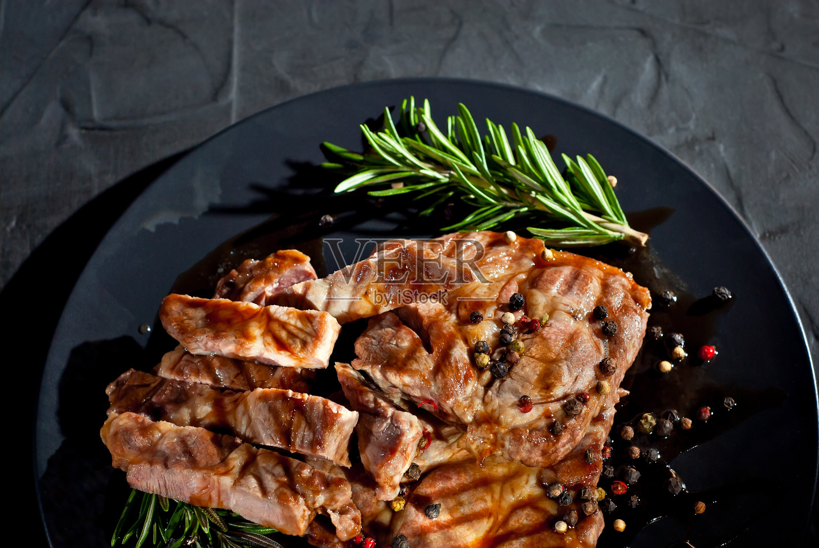 黑色盘子上的酱汁牛排。肉与香料和迷迭香在黑暗的背景。对比光线作为艺术效果。照片摄影图片