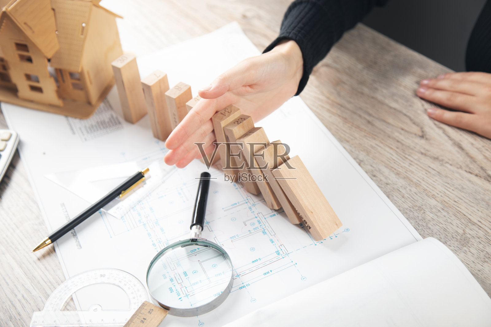 手阻止木制多米诺骨牌掉在木制房子模型上照片摄影图片