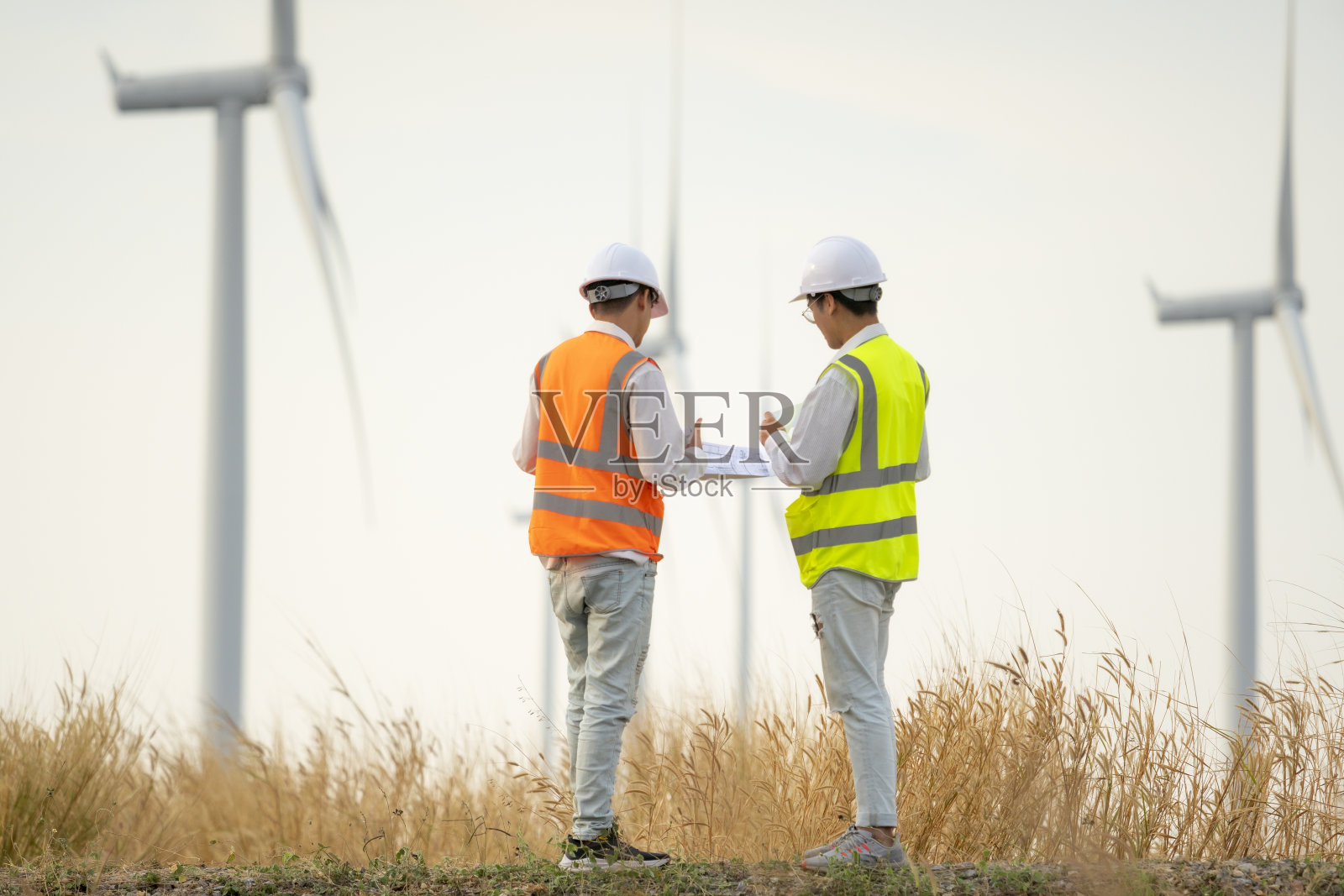 两名身穿制服的亚洲工程师或技术员讨论和检查。风力涡轮机生态能源工业发电风车现场工人可再生背景。照片摄影图片