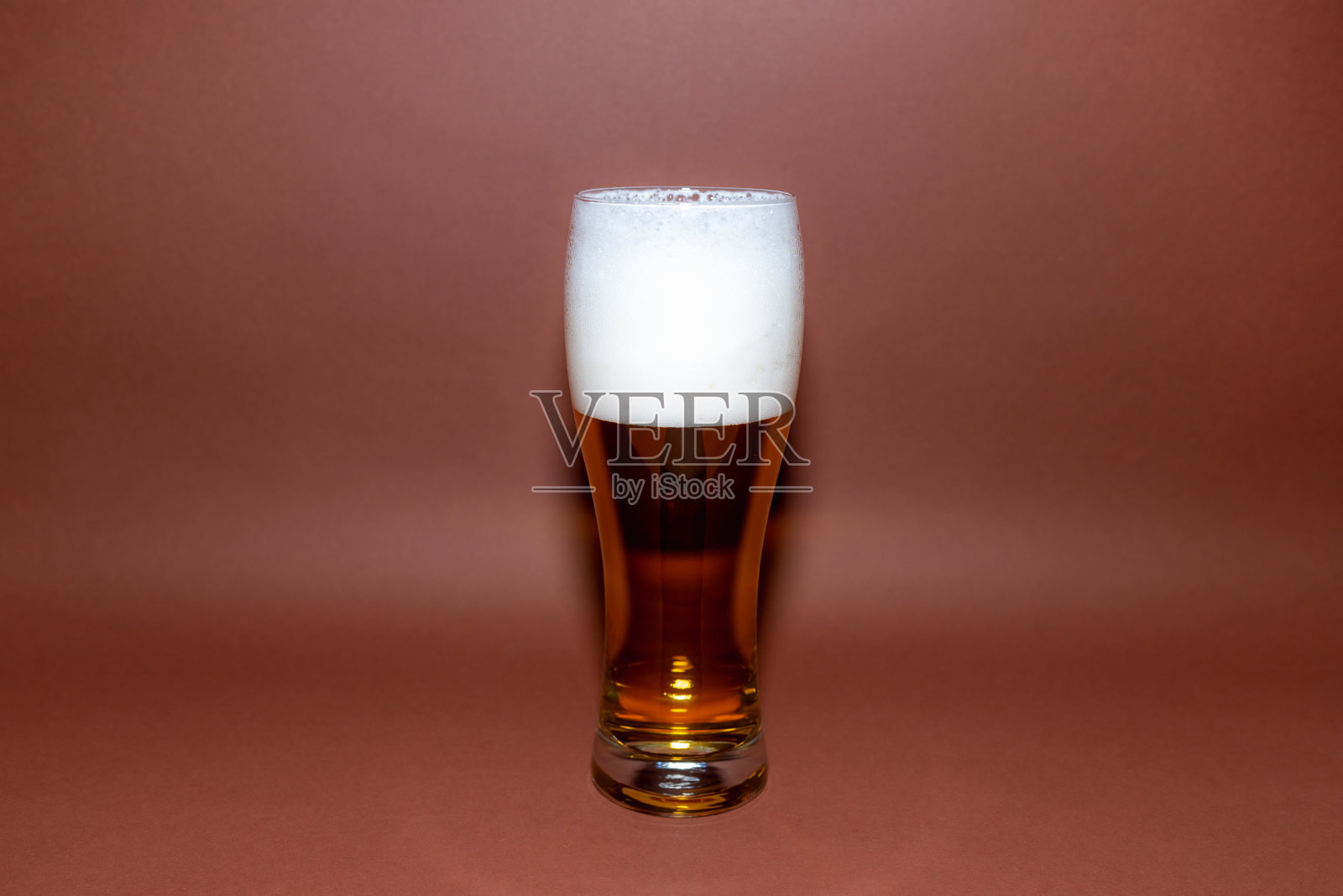 一杯啤酒在棕色背景与复制空间。琥珀色玻璃泡沫啤酒。棕色的背景。有选择性的重点。照片摄影图片
